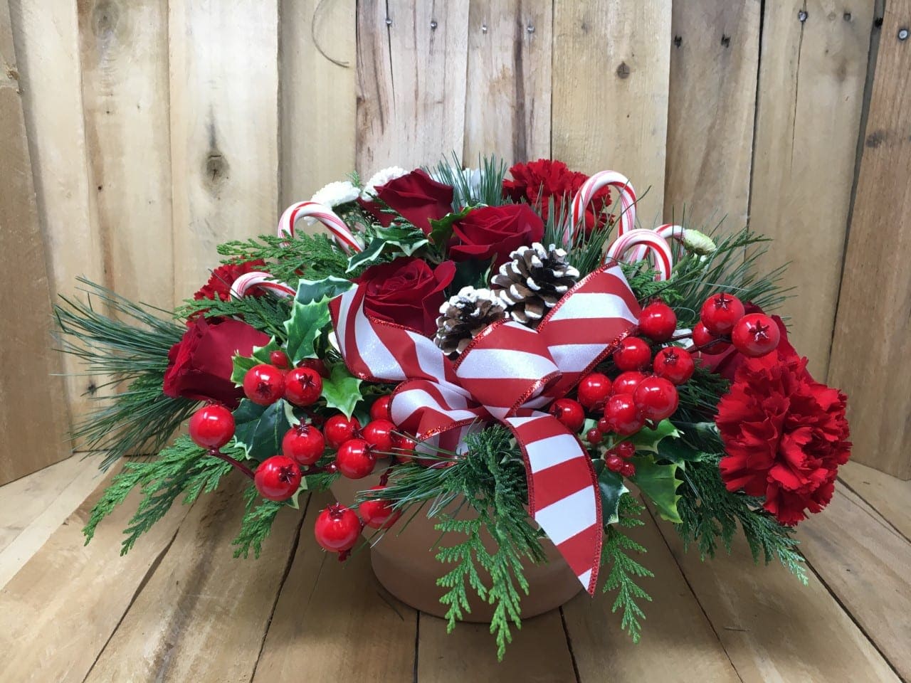 Candy Cane Christmas - Add some Holiday Cheer with this bright and festive arrangement! Traditional colors and flowers in this arrangement include roses, carnations, and floral pomps that are accented with fragrant evergreens, pine cones, and ribbon.