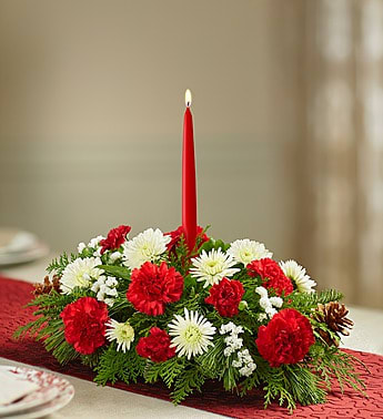 Warm Wishes Christmas Centerpiece - Every family has its own holiday traditions. Let us help you add one more with our classic Christmas centerpiece. Beautifully arranged using fresh blooms in the signature colors of the season, white lilies, red roses and more this lively display is accented with a fragrant mix of evergreens and pinecones. And for a finishing touch, our florists add a red taper candle, creating a warm and festive glow for all your celebrations!