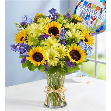 Fields Of Europe For Dad - Our summertime best seller is designed to celebrate every amazing dad. Gathered with fresh-picked blooms in shades of blue and yellow, this rustic arrangement is paired with a colorful Father’s Day balloon. Whether you’re home together or sending wishes from a distance, it’s a gift rich in sentiment for the man who means so much. All-around arrangement with sunflowers, blue delphinium, yellow daisy poms, green button poms and purple statice; accented with assorted greenery Artistically designed in a clear glass vase accented,raffia; with a Father’s Day Mylar balloon