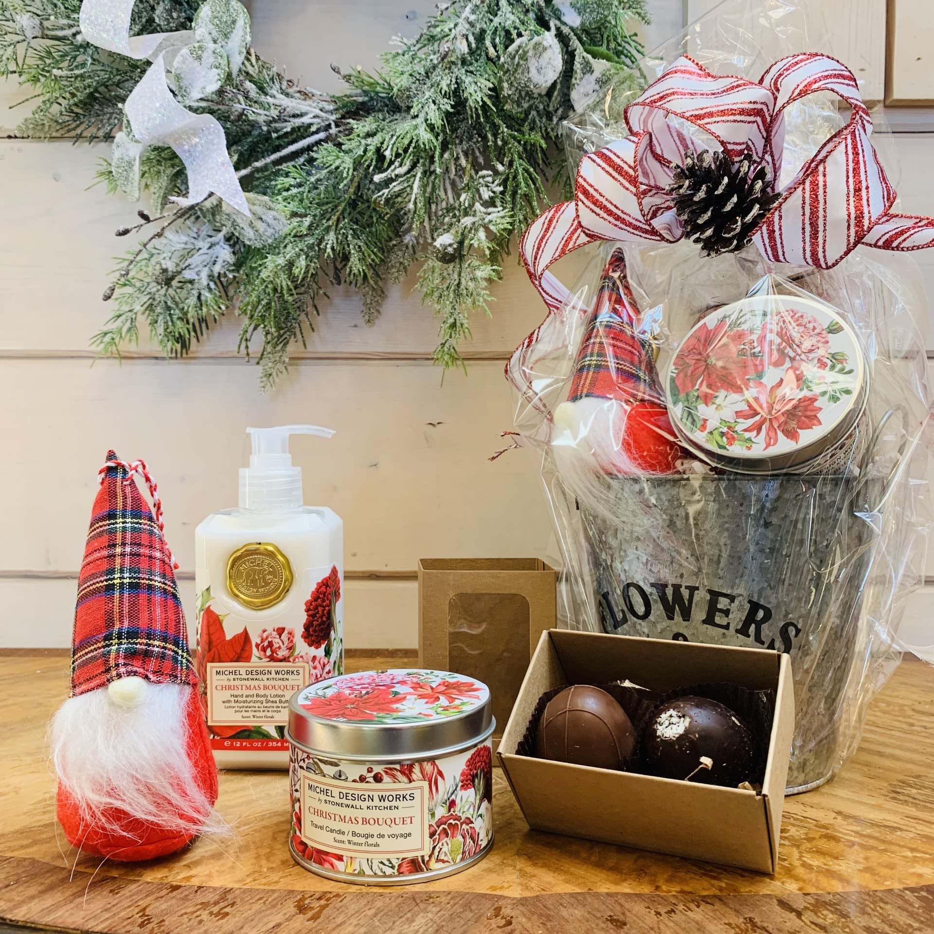 Christmas Bouquet Gift Basket - Standard - This standard Christmas Bouquet gift basket includes a gnome, a two piece box of chocolates, one hand and body lotion and one scented travel candle beautifully wrapped up and ready to go with a large bow and pinecone accent.  Fragrance: Winter florals with notes of red fruit, jasmine, and lavender  Items included: 1)	a hand picked just for you Christmas gnome ornament with a $4.95 value  2)	A two piece box of our specialty chocolate truffles made in the USA from imported Belgian chocolate. Pictured flavors are milk chocolate and coconut, substitutions available on request, or occasionally necessary due to supply.  Contains nuts.  3) Our hand and body lotion is made with shea butter, aloe, and other botanical ingredients and packaged in a decorative pump bottle. 12 fl. oz. / 354 ml lotion.  4) Our all-natural, travel candle is nontoxic, biodegradable and clean burning, made from a sustainably sourced soy and palm oil wax blend. The handy, decorative, and versatile tin can be used at home or when traveling, indoors or out. 5.5 oz./ 155 g. Over 20 hrs. approximate burn time.  Customizable gift baskets available upon request. Please give us a call at 775-348-6161 for assistance putting together the perfect aromatherapy basket for your loved one. 