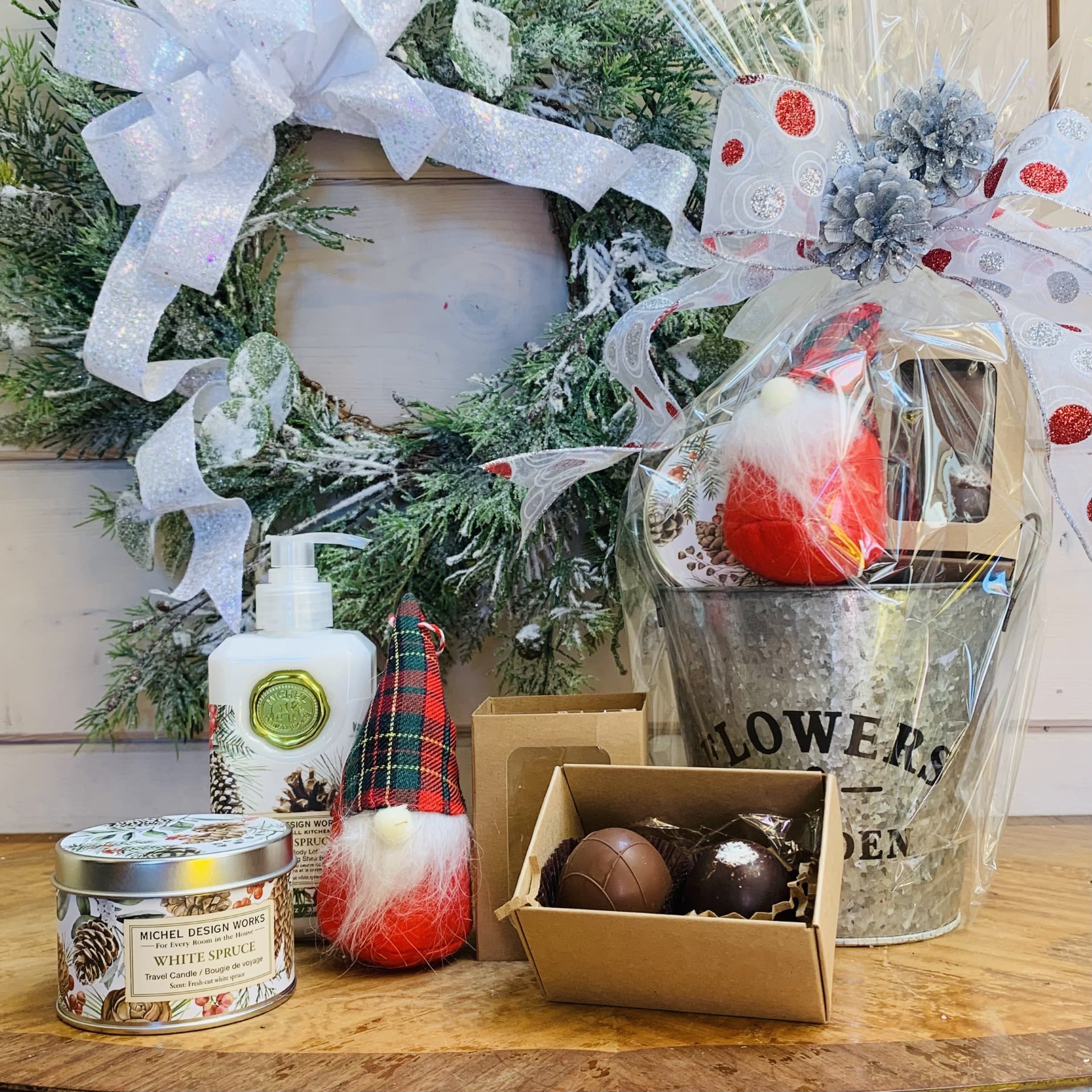 White Spruce Gift Basket – Standard - This standard White Spruce gift basket includes a gnome, a two piece box of chocolates, one hand and body lotion and one scented travel candle beautifully wrapped up and ready to go with a large bow and pinecone accent.  Fragrance: True Spruce with touches of fruit and spice  Items included: 1)	a hand picked just for you Christmas gnome ornament with a $4.95 value  2)	A two piece box of our specialty chocolate truffles made in the USA from imported Belgian chocolate. Pictured flavors are milk chocolate and coconut, substitutions available on request, or occasionally necessary due to supply.   3) Our hand and body lotion is made with shea butter, aloe, and other botanical ingredients and packaged in a decorative pump bottle. 12 fl. oz. / 354 ml lotion.  4) Our all-natural, travel candle is nontoxic, biodegradable and clean burning, made from a sustainably sourced soy and palm oil wax blend. The handy, decorative, and versatile tin can be used at home or when traveling, indoors or out. 5.5 oz./ 155 g. Over 20 hrs. approximate burn time.  Customizable gift baskets available upon request. Please give us a call at 775-348-6161 for assistance putting together the perfect aromatherapy basket for your loved one. 