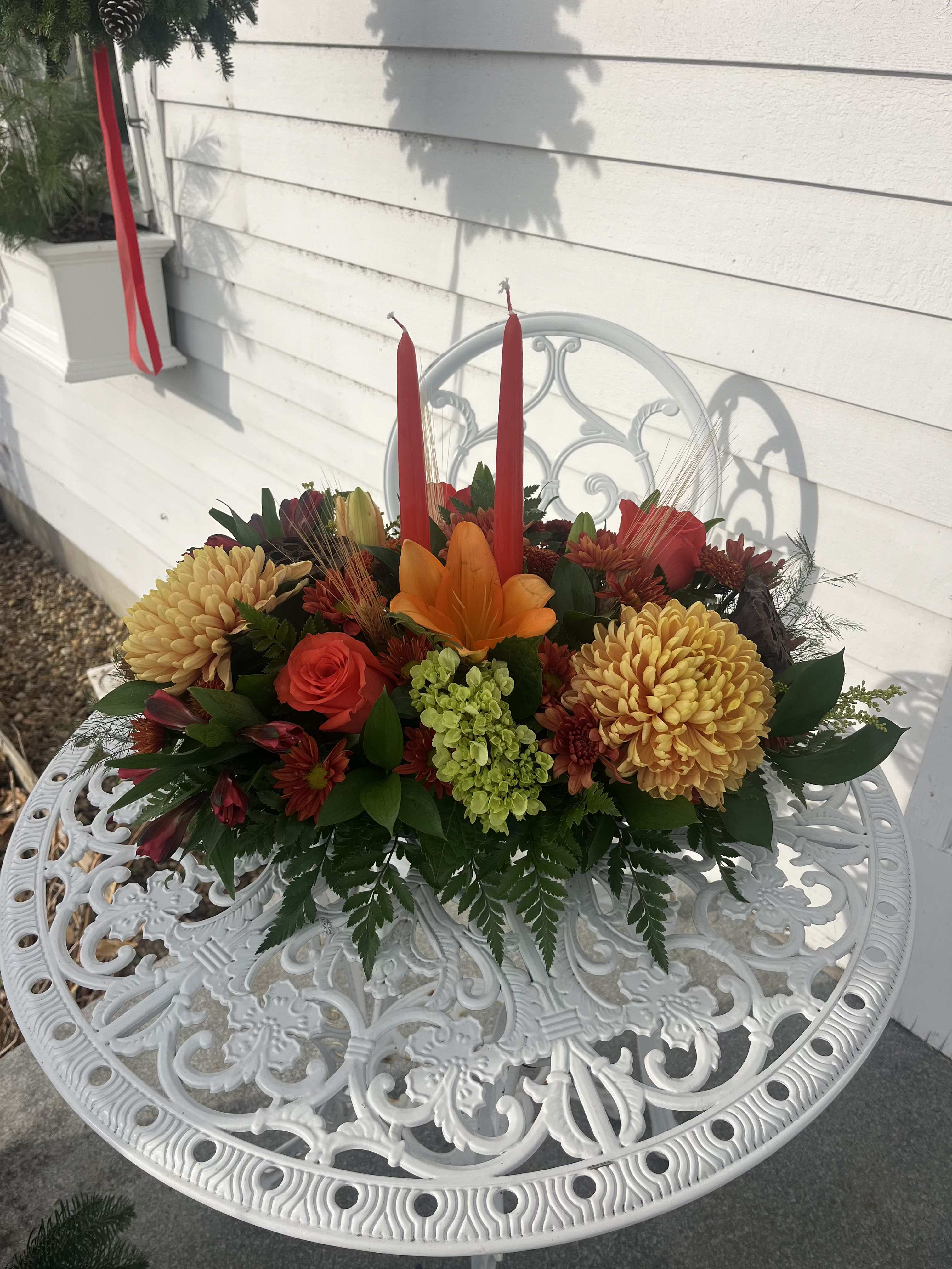 Turkey Day Petal Parade Centerpiece - Orange lilies, roses, green hydrangea, fall cremons,  fall daisies and chrysanthemums with wheat and 2 taper candles designed long and low.
