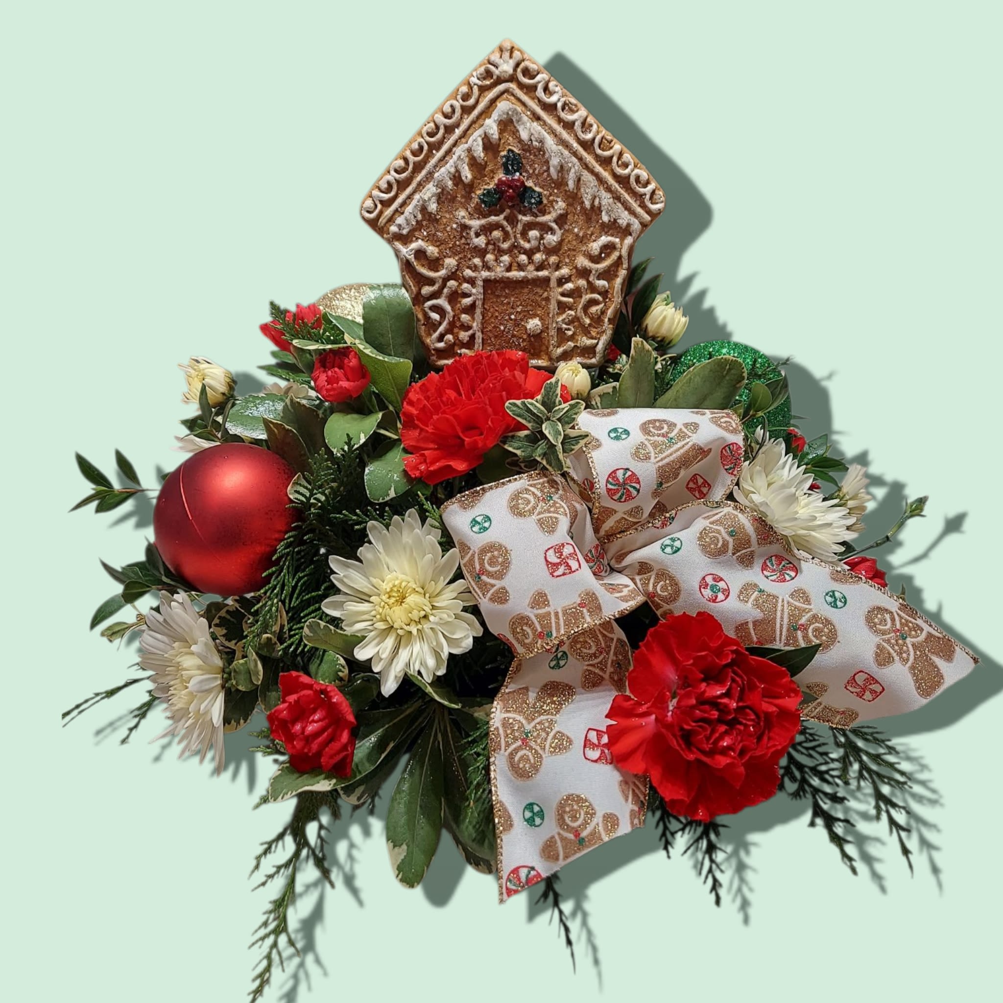 GIngerbread Cookie Bouquet - Our Gingerbread Cookie Bouquet will be a sweet treat for everybody! A gingerbread house is set in the middle of wintergreens, holiday blooms and bulbs. APPROXIMATE size: 13&quot;W x 11&quot;H