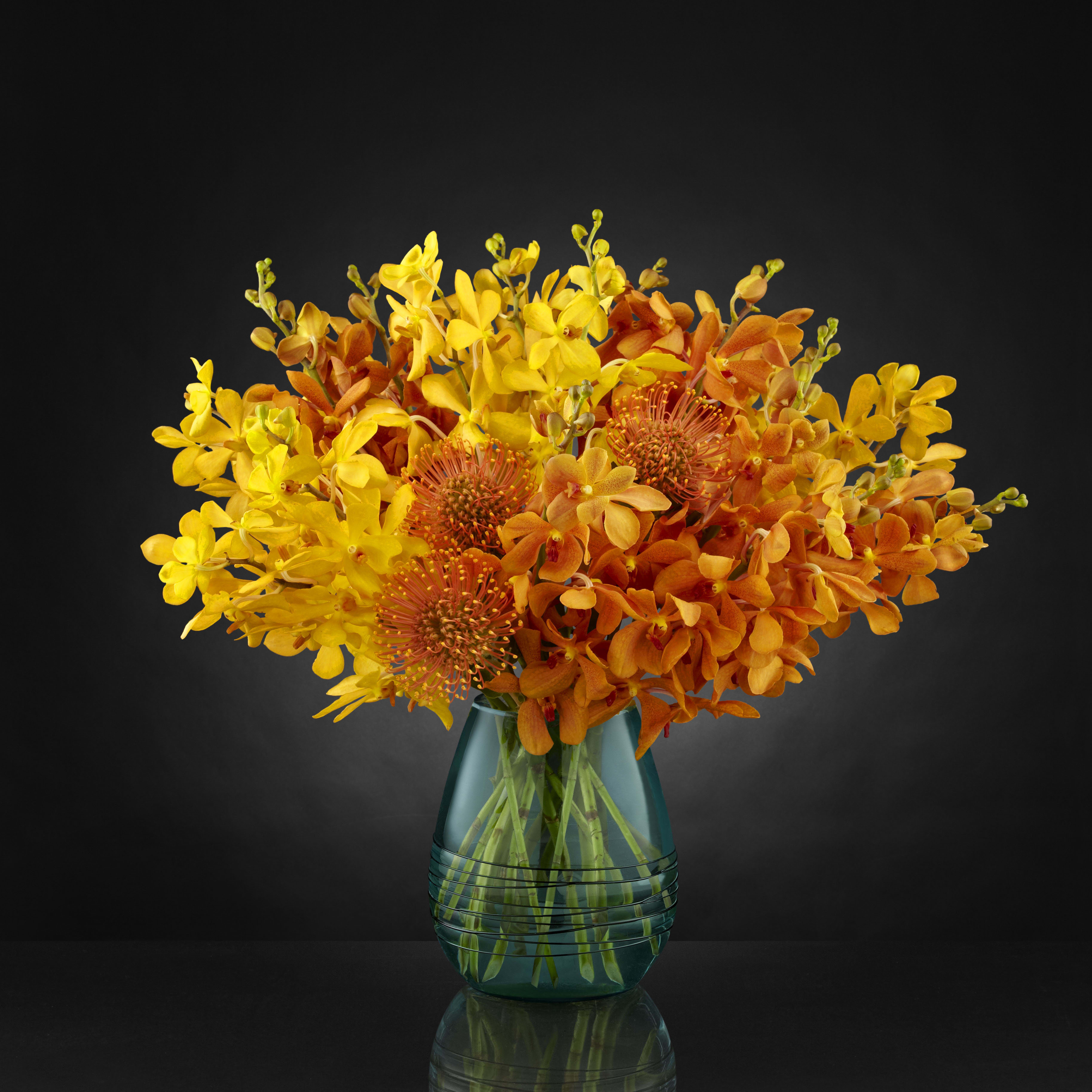 Desert Skies Bouquet - Orange and gold Mokara orchids and bright pin cushion protea. Same day delivery may not be available depending on orchid color availability. Vase may be different, but size will be appox 7&quot; tall by 4&quot; wide, overall arrangement is 15&quot; tall and approx 20&quot; wide. 