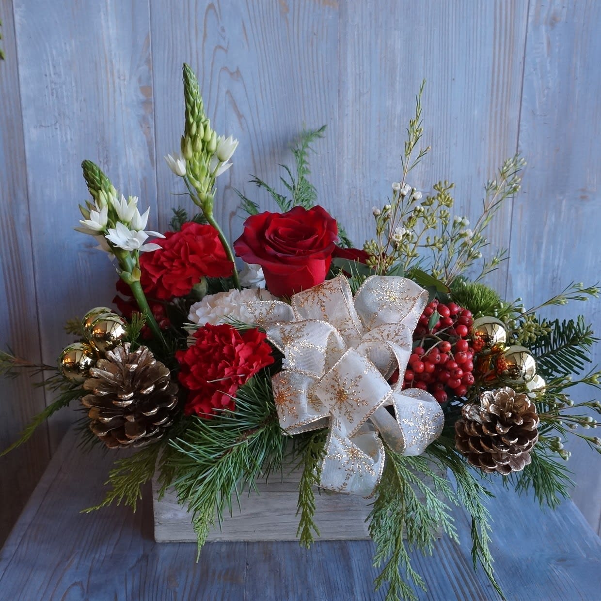 Woodland Traditions - Traditional Christmas arrangement consisting of lush red roses, star of Bethlehem and waxflower, accented with pine cones, balls, and ribbon. All nestled in a wooden box. 
