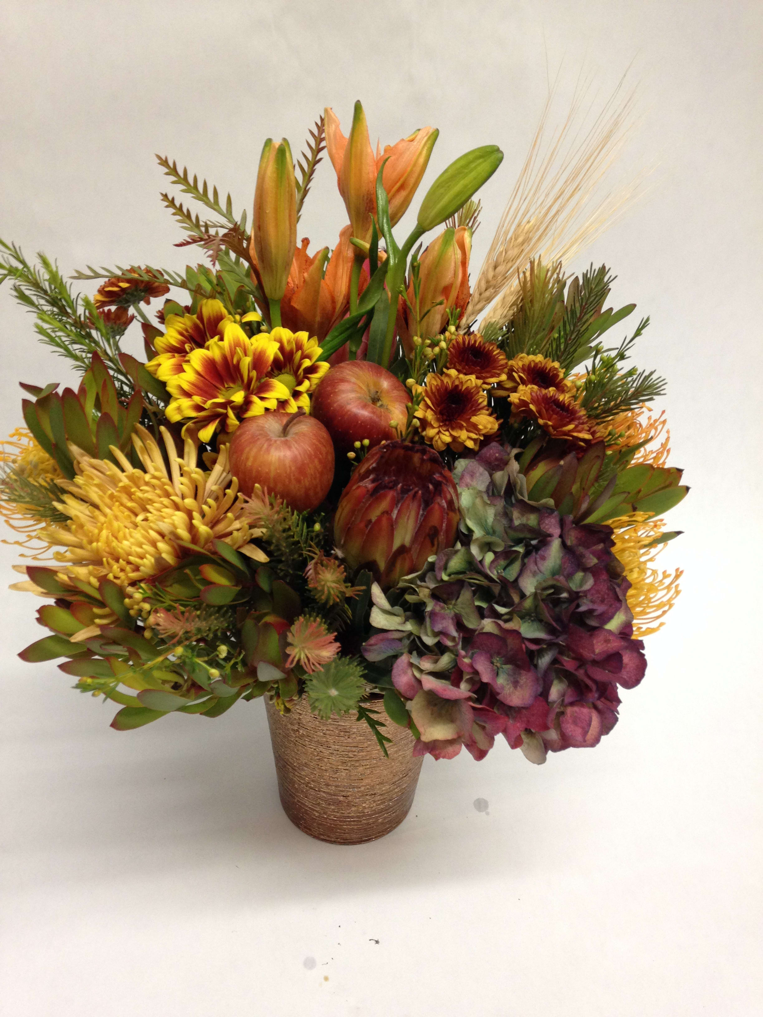 Autumn Harvest - This autumnal inspired arrangement comes complete with asiatic lilies, spider mums, safari branches, mums, pin-cushion proteas, proteas, seasonal fruit and various seasonal greenery.  (Some flowers may be subject to change depending on the season. We will contact you with available flower substitutions; please contact us with specific questions if you are concerned with flower availability, thanks!)  Featured arrangement: 125.75 (Regular Price)