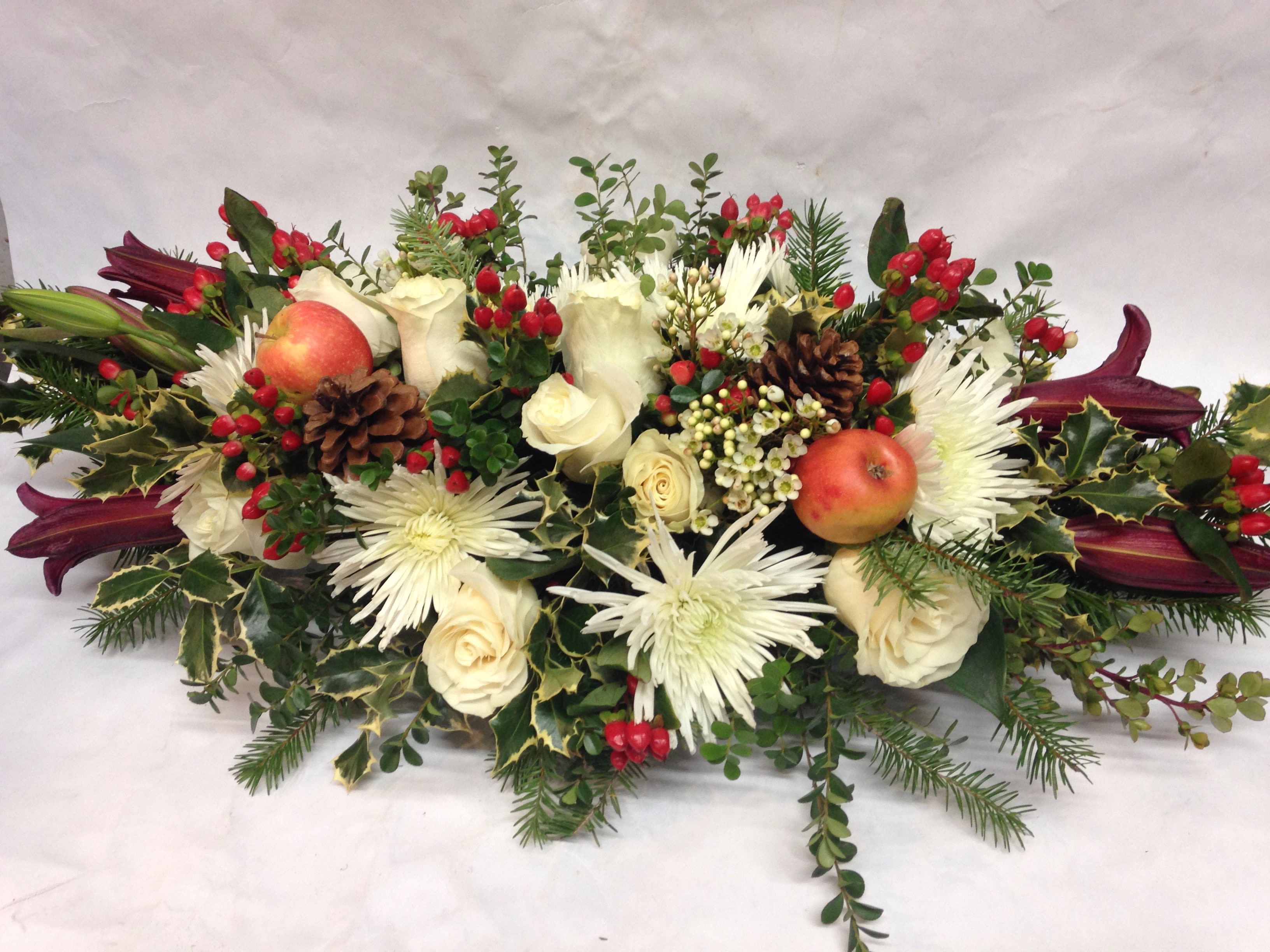 Long Winter Centerpiece - This lush centerpiece will make a statement at your next dinner party or holiday event. The two foot long arrangement includes white roses, winter spider mums, burgundy lillies, plenty of winter greens, and even an apple or two! Featured Arrangement: $445.00
