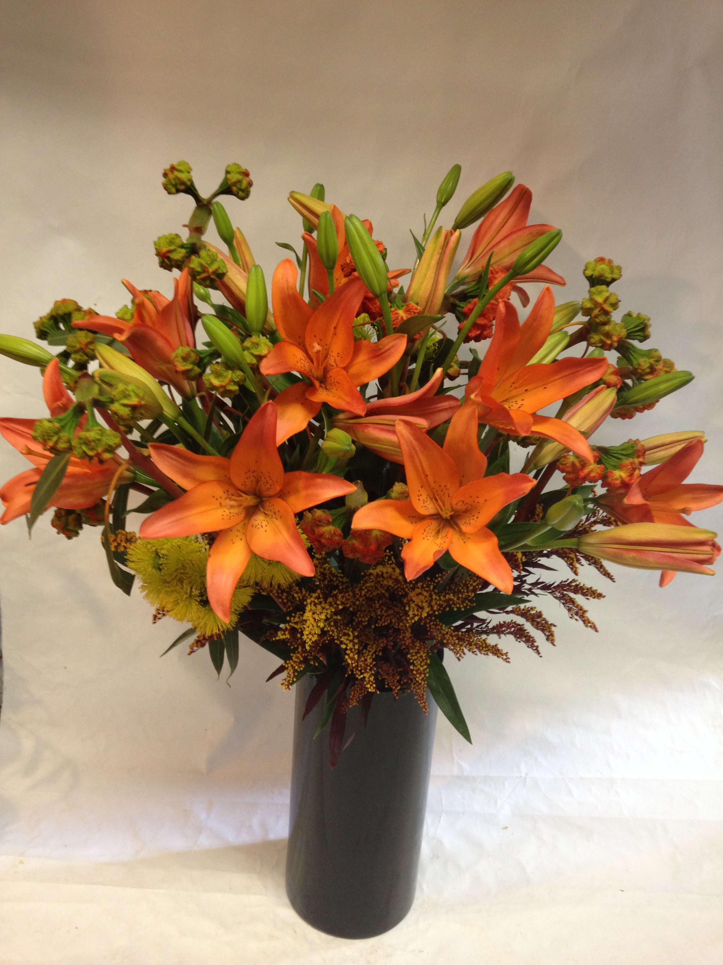 Modern Autumn Harvest   - This array of festive tiger lilies, eucalyptus, solidago and greenery comes in a sleek black ceramic vase. Beautiful for an office, entryway, or a remembrance to a friend. (Some flowers may be subject to change depending on the season. We will contact you with available flower substitutions; please contact us with specific questions if you are concerned with flower availability, thanks!)  Featured Arrangement: $185.00 
