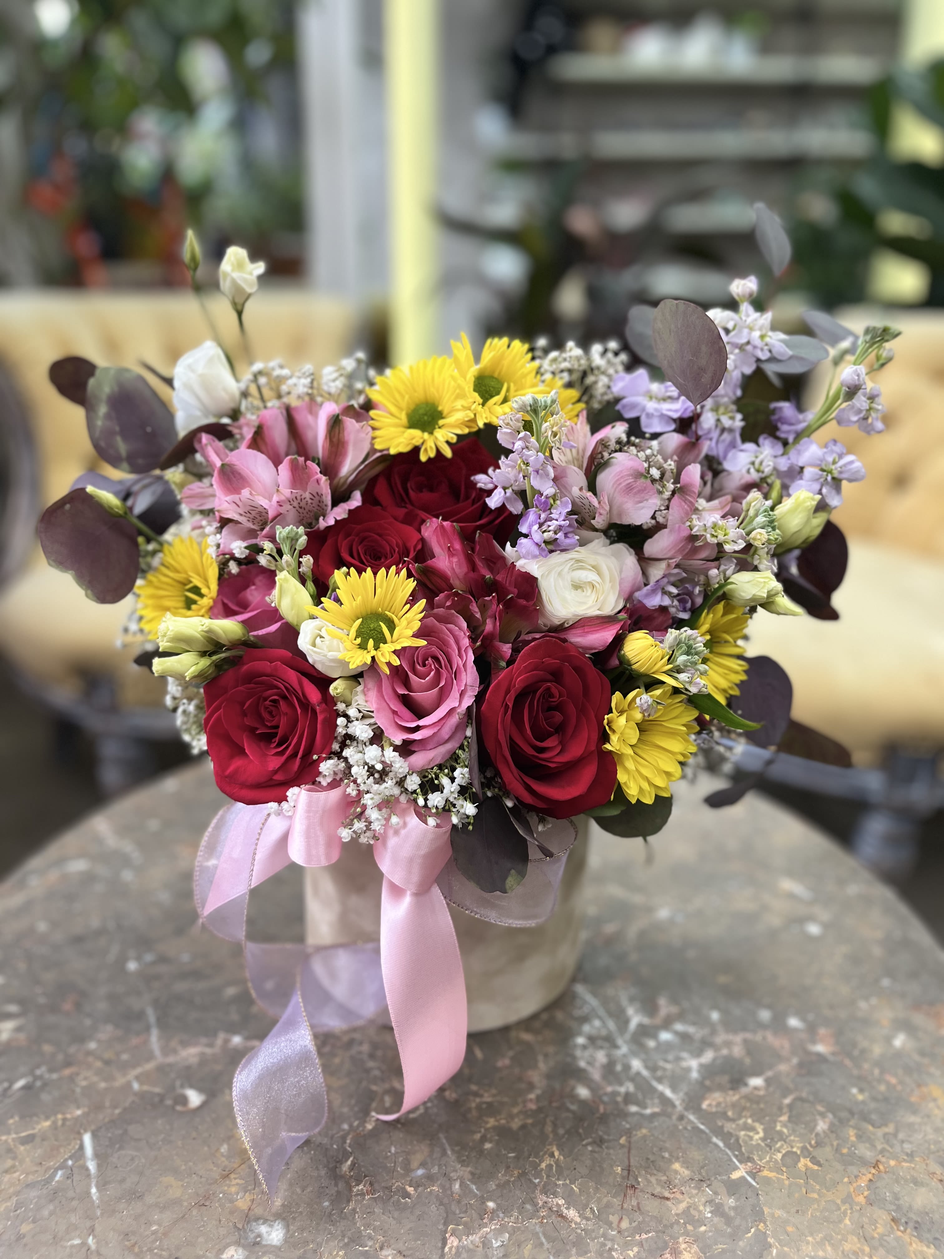 Rosy Glow - A joyful garden of color in full bloom — featuring classic red and blush roses, sunny yellow daisies, lilac stock, alstroemeria, and soft touches of baby’s breath. Designed in a marble-textured vase and finished with a pink satin bow, this arrangement brings warmth and happiness to any space. Perfect for birthdays, thank-yous, or just because.