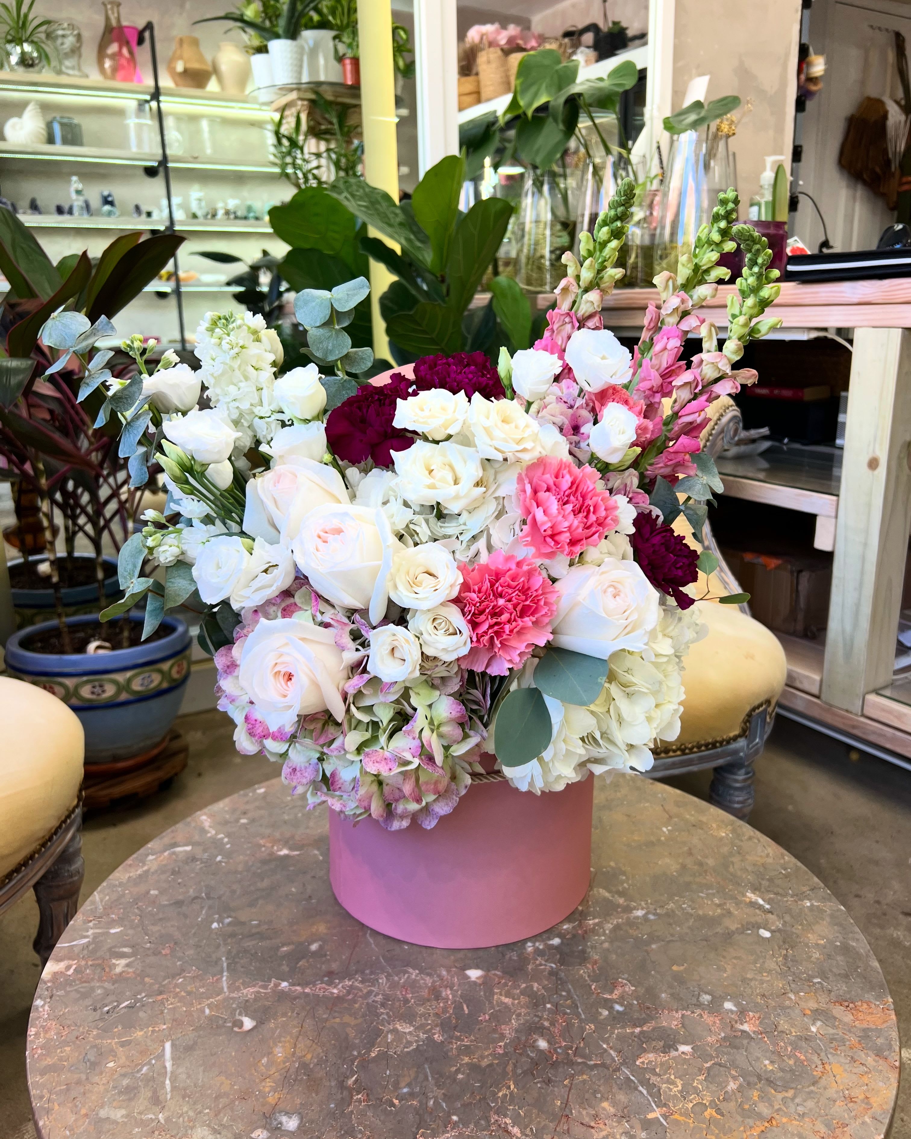Signature Pink Hatbox - A lush, romantic arrangement designed in our signature pink hatbox. Filled with premium roses, spray roses, hydrangea, carnations, snapdragons, and soft eucalyptus, this piece makes an elegant statement for any celebration.