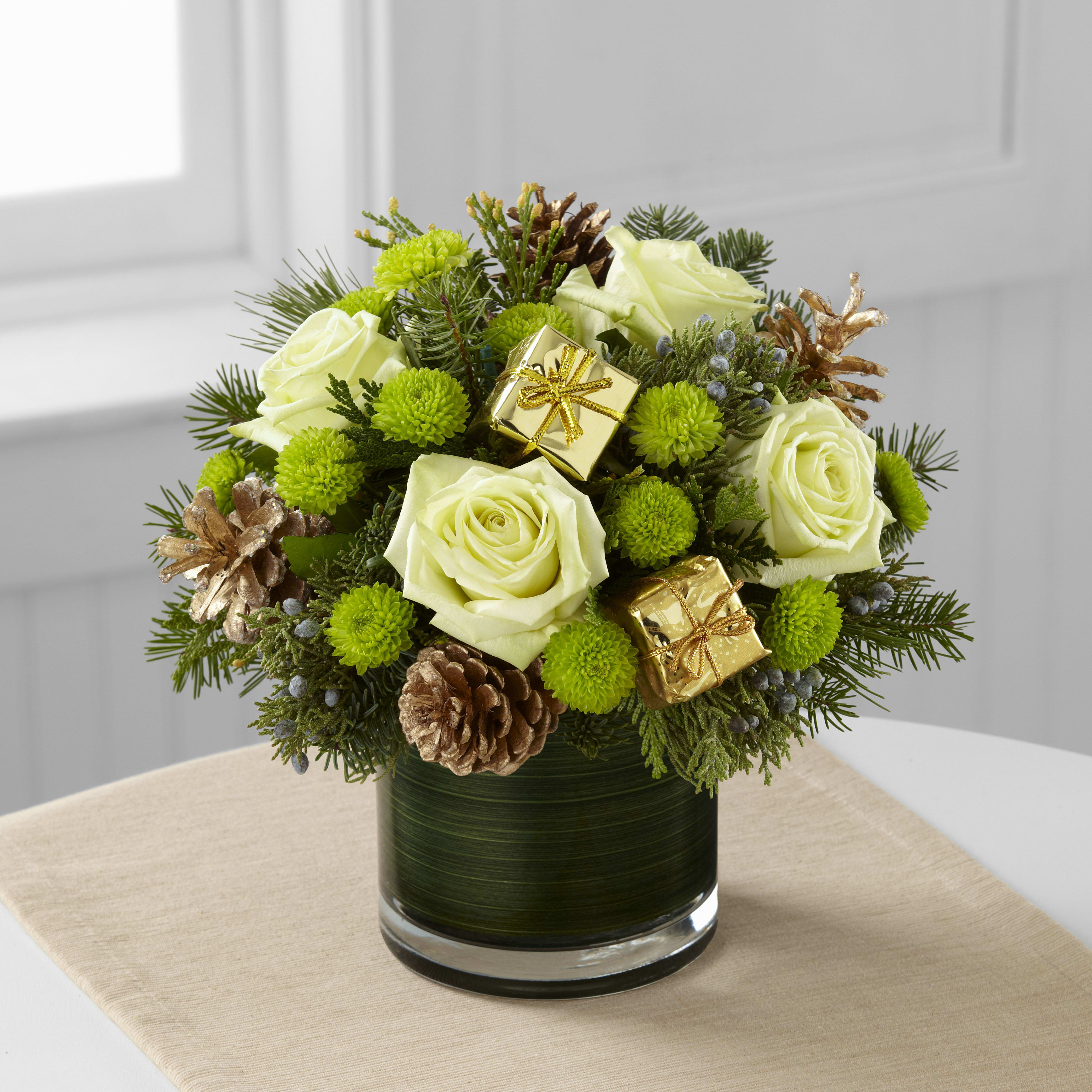 Season's Sparkle - Season's Sparkle brings an elegance and sophistication to the holiday season with it's natural elements and style. Jade green roses are stunning surrounded by green button poms, assorted holiday greens, gold tipped pinecones and gold present pics to create an impressive fresh flower arrangement. Presented in a clear glass cylinder vase lined with ti green leaf material to give it a polished finish, this holiday flower bouquet is set to make the perfect impression on any of the special people on your Christmas gift list.