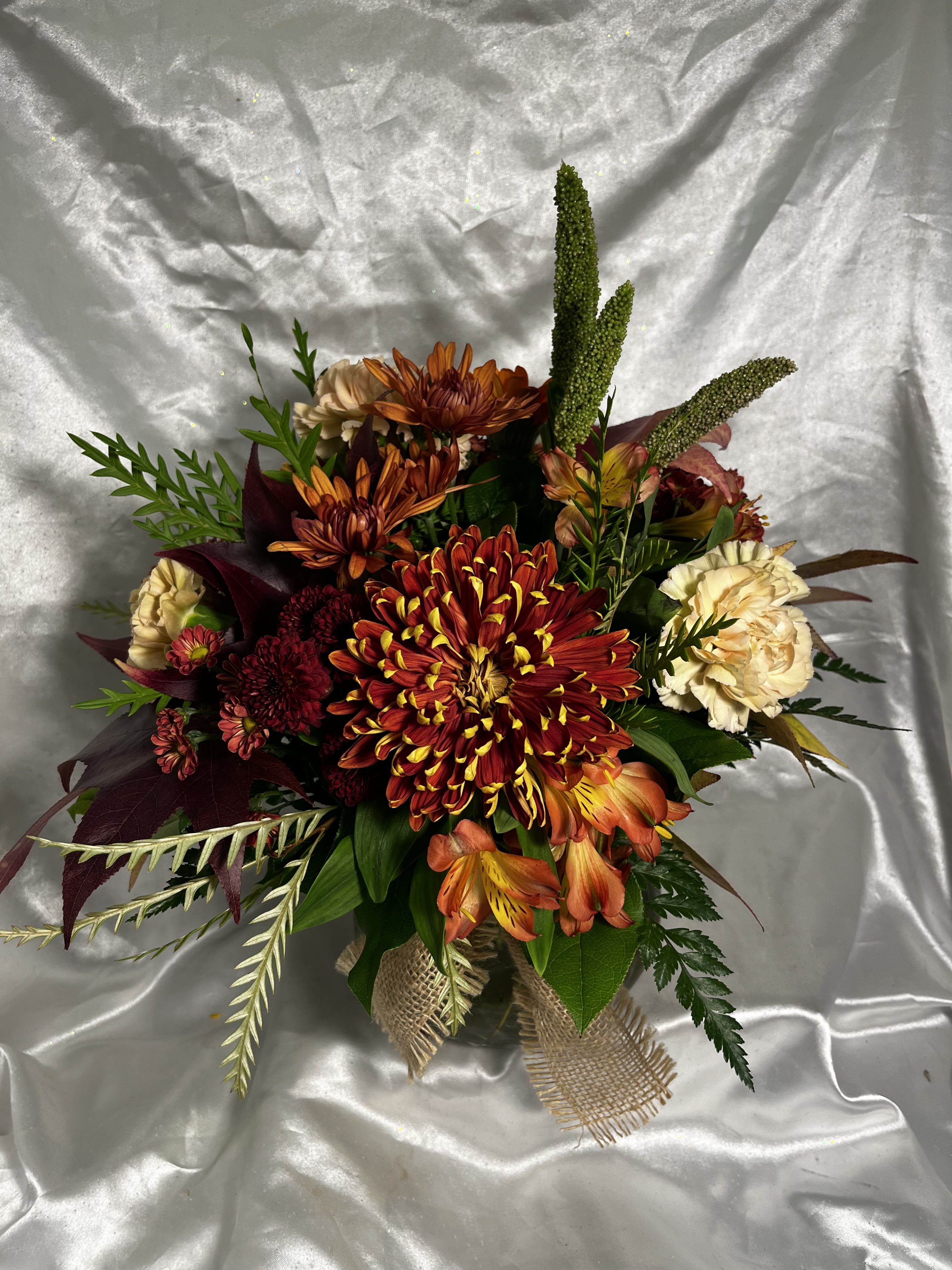 Donna's Amber Ambience - Oranges, reds and ambers greet you in this delightful Fall arrangement, complete with a quaint burlap accent.  Who could go wrong with Fuji Mums, Alstromeria, and sweet Carnations?  Quite the heartwarming array to share with loved ones!