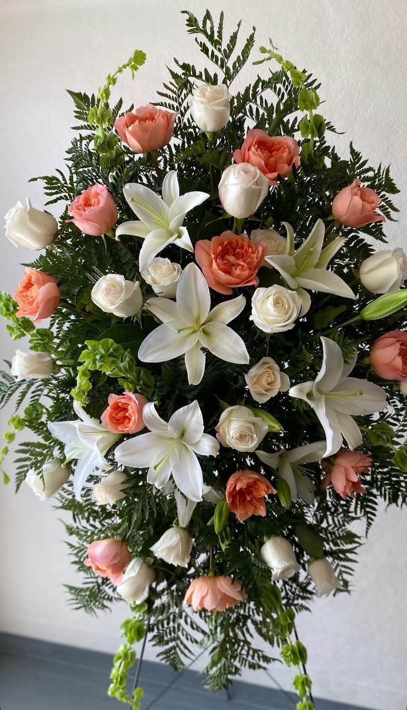 Peach &amp;White Grace Standing Spray  - This peach and white standing spray is a graceful expression of warmth, purity, and heartfelt remembrance. Soft peach blooms symbolize gratitude and comfort, while white flowers bring a sense of peace and eternal love. Arranged with delicate greenery and uplifting accents, this standing spray offers a serene and comforting presence at the service. It honors your loved one with beauty, tenderness, and a timeless tribute of compassion.