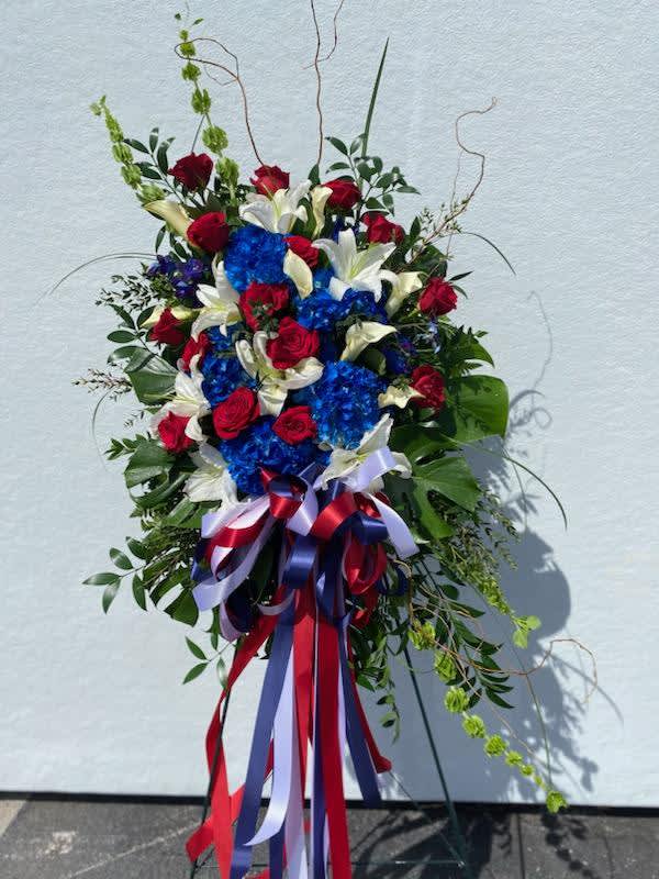 Heavenly Salute - A full and fresh standing spray filled with assorted red, white, and blue flowers. A perfect addition to any service member's memorial service. Adorned with a huge patriotic bow. 