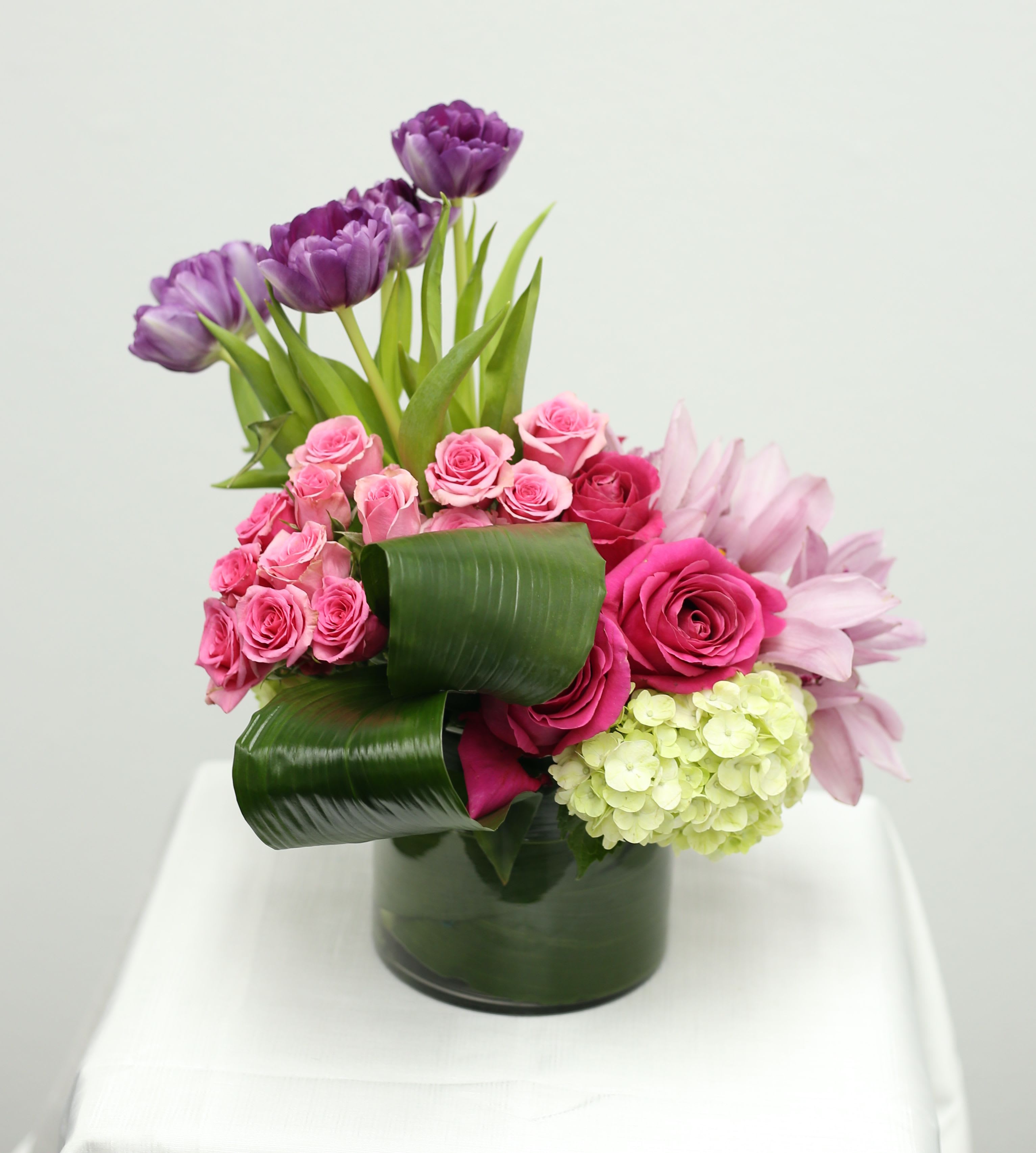 Vibrant Blooms - Make their day with this exquisite floral centerpiece. Featuring a carefully selected mix of Tulips, Garden Roses, and Hydrangeas creating a warm and inviting display. The modern glass vase adds a touch of elegance. Perfect for tables, shelves, or as a thoughtful gift. 
