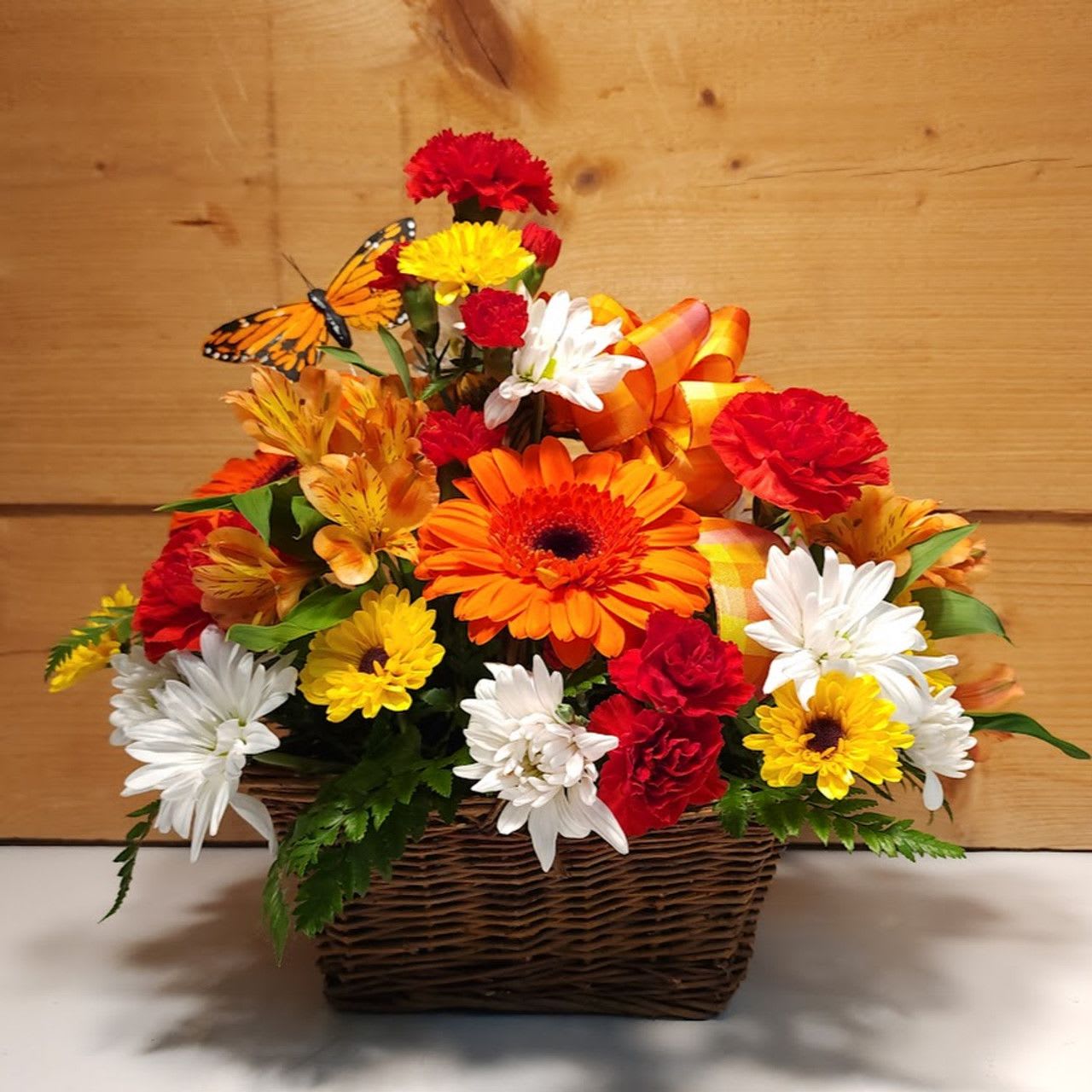 Bright Beauty Butterfly Basket - The Bright Beauty Butterfly Basket is a wonderful presentation of Carnations, Mini Carns and a butterfly pick highlighted by daisies, yellow vikings and orange alstroemeria all featured in a basket with a bow.  Approx 14&quot; H x 12&quot; W