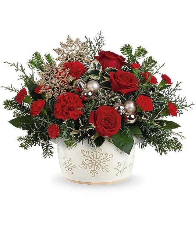 Snowflake Symphony - Red flowers and bright pops of gold makeup Snowflake Symphony. Flowers like roses, carnations, and mini carnations are nestled among long-lasting evergreens. Golden snowflakes and ornaments dance across the arrangement in a symphony of Christmas spirit. The flowers are designed in a low and compact style that is perfect for a holiday centerpiece. Snowflake Symphony features a food-safe stoneware crock with golden snowflakes. Send Snowflake Symphony as a Christmas gift or bring this arrangement along for the host of your next holiday party.