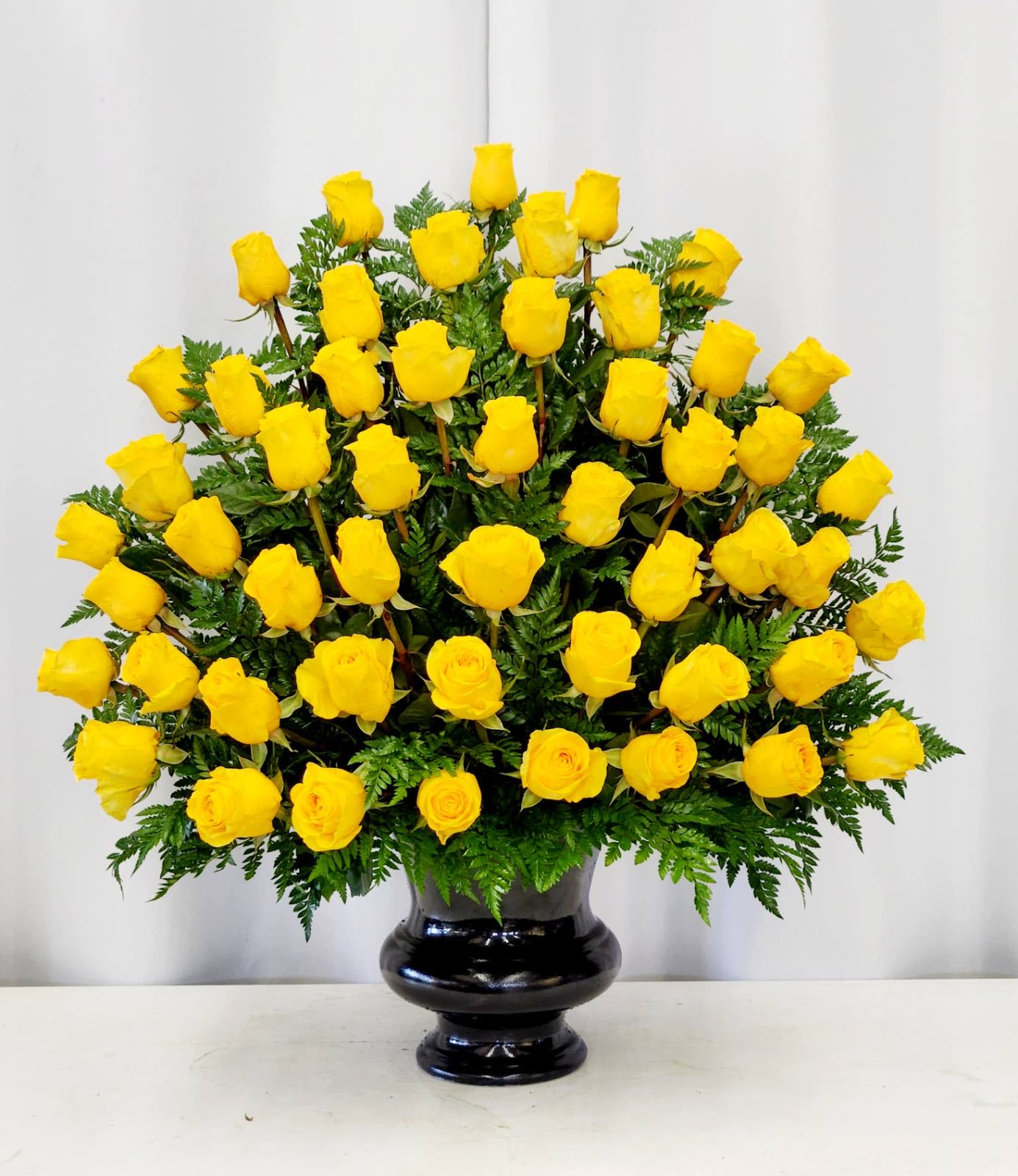 Memories of You - Brighten any moment with this stunning arrangement of four dozen vibrant yellow roses, artfully spread wide and tall to create maximum impact. Lush green accents add depth and movement, while the sleek black vase provides a sophisticated contrast that lets those golden blooms steal the show. Perfect for celebrations, apologies, or simply reminding someone they're unforgettable. Ideal for memorial and grand opening of business.  Approximate Size:&nbsp;  Standard: 18&quot; x 20&quot; 2 DOZEN  Deluxe: 20&quot; x 24&quot; 3 DOZEN  Premium - As Pictured: 25&quot; x 32&quot; 4 DOZEN