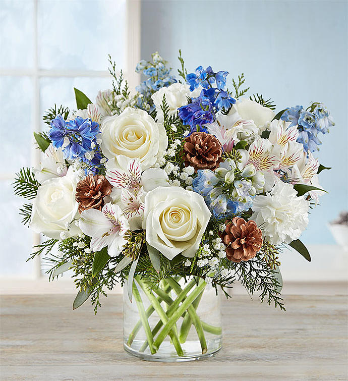 Winter Wishes Bouquet™ - Inspired by winter’s cool white and blue landscape, our delightful arrangement delivers your warm wishes to the people you love. Hand-designed with a lush gathering of blooms, evergreens and rustic touches, it’s a thoughtful expression of the season’s natural beauty. All-around arrangement with white roses, carnations and Peruvian lilies (alstroemeria); blue delphinium; accented with baby’s breath, seeded eucalyptus, assorted Christmas greenery and pinecones