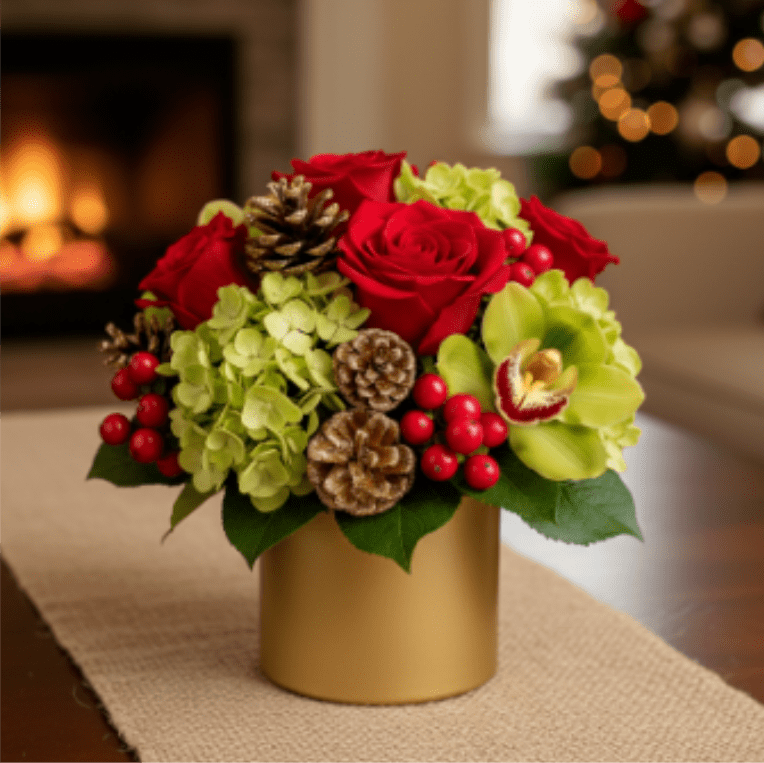 Yuletide  - Capture the spirit of the season with our stunning Gilded Yuletide Luxury arrangement. This sophisticated and compact design is the ultimate expression of holiday elegance, combining classic red and green with the opulent shine of gold. It makes a magnificent accent piece for a desk, coffee table, or as a thoughtful gift. The Container: A chic, contemporary metallic gold cylinder vase serves as the perfect vessel, providing a rich, modern backdrop for the colors.  Luxurious Blooms:  Velvety Red Roses: Deep, vibrant red roses anchor the arrangement, symbolizing holiday love and joy.  Exotic Cymbidium Orchid: A graceful, lime-green Cymbidium orchid bloom adds unexpected texture, height, and a touch of tropical luxury.  Chartreuse Hydrangea: Clusters of pale, apple-green hydrangea fill the base, providing lush volume and a crisp color contrast.