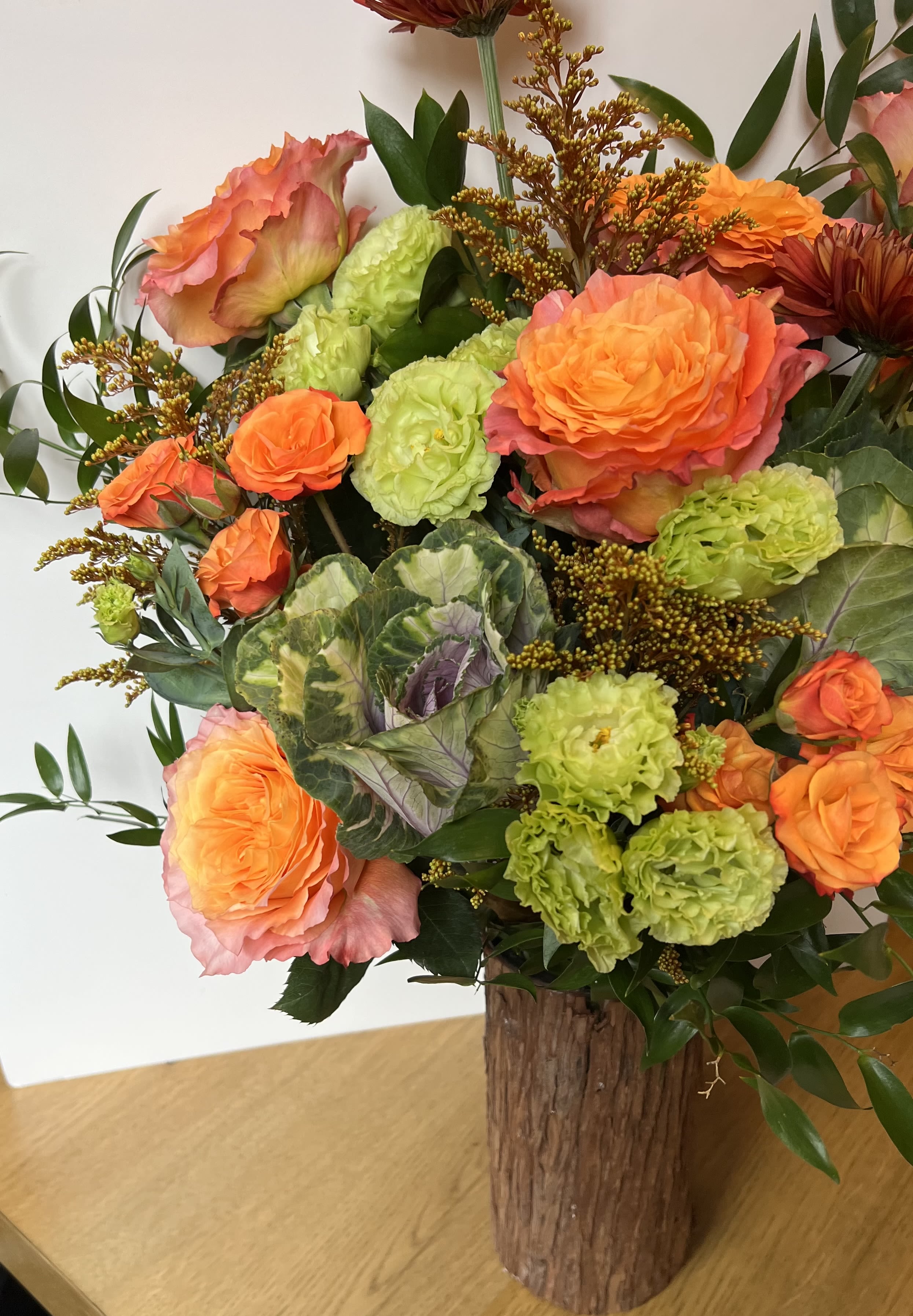 Thankful Tree - Vibrant and capturing the warm hues of the autumn season. Designed in a rustic wood-textured vase, it features a lush blend of tangerine roses, lime-green lisianthus, ornamental kale, sunset-toned garden roses, and accents of golden seasonal filler.