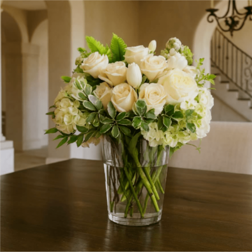 A Glowing Elegance  - A Glowing Elegance – White Roses, Tulips, Hydrangeas &amp; Lisianthus in a Clear Vase Elevate any space with A Glowing Elegance, a luxurious floral arrangement in a crystal-clear vase. This captivating bouquet showcases pristine white roses, fragrant tulips, lush hydrangeas, and delicate lisianthus, artfully accented with fresh, vibrant greenery. Perfect for weddings, anniversaries, or special celebrations, this timeless arrangement exudes sophistication and grace, leaving a lasting impression on anyone who receives it.
