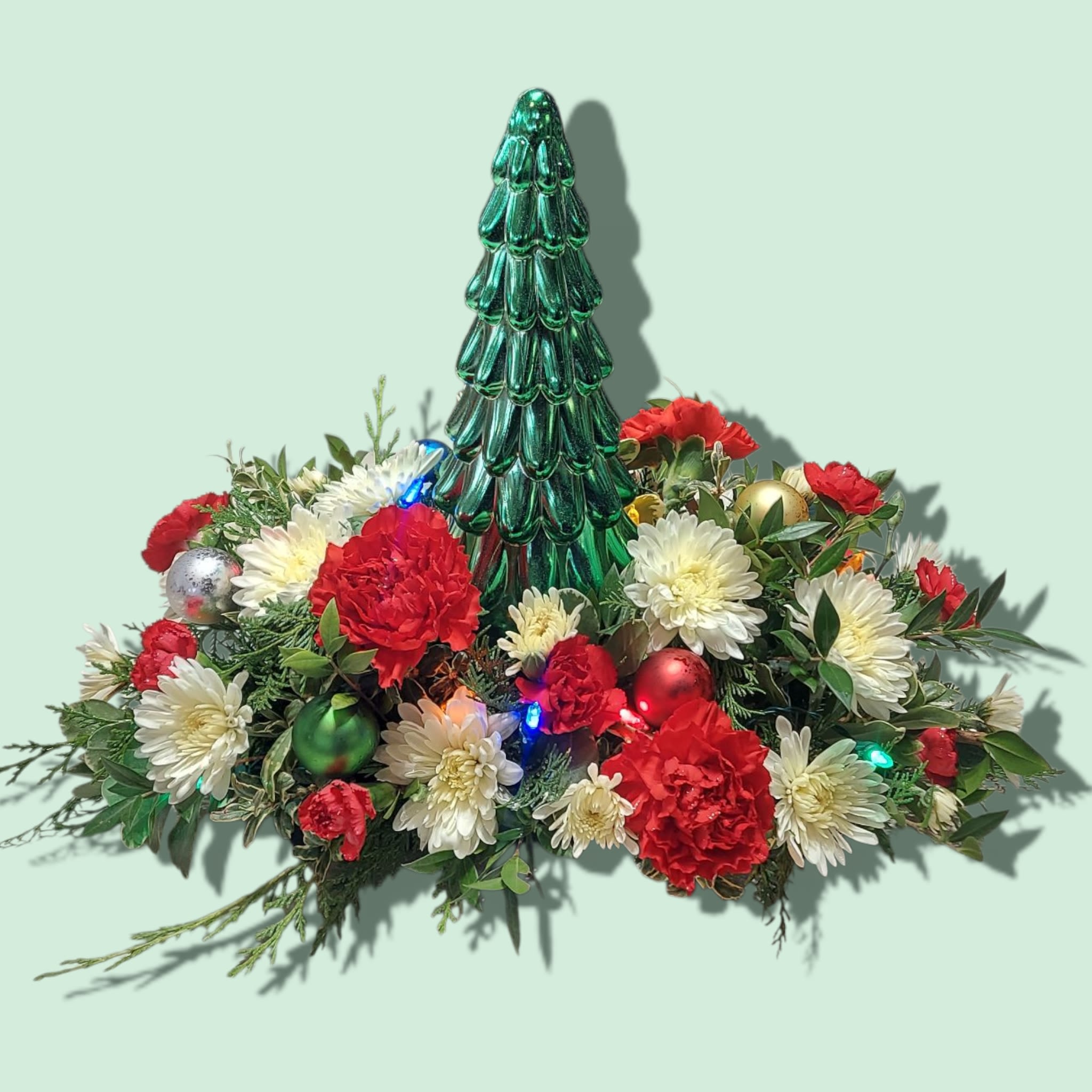 O' Christmas Tree - A festive arrangement centered around a metallic colored tree. A string of battery powered, timer lights and mini ornaments adorn the classically colored centerpiece of red carnations and white mums. Approximate size: 17&quot; W x 12&quot; H COLORS OF TREES WILL VARY BETWEEN SILVER, GOLD, AND GREEN.