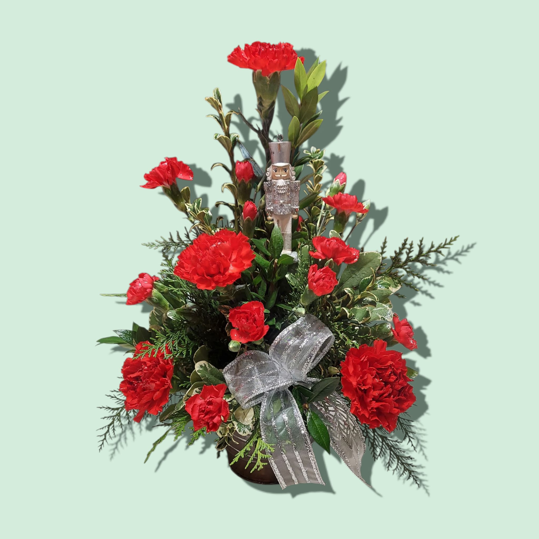The Nutcracker Suite - The Nutcracker Suite features a keepsake ornament nestled among winter greens and red carnations. COLORS OF CONTAINER AND ORNAMENT WILL VARY WITH AVAILABILITY. Approximate size: 16&quot;H x 11&quot;W