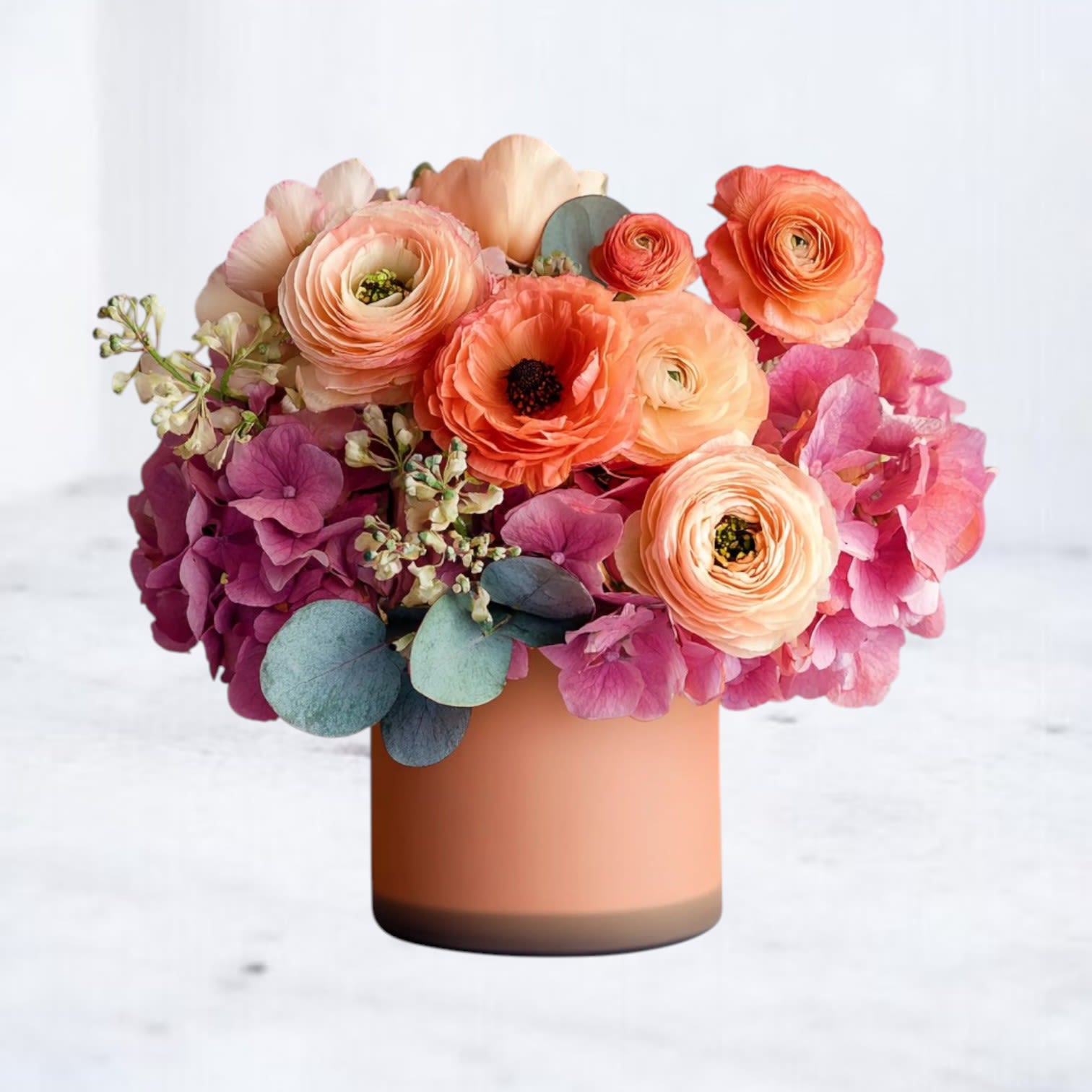 Honeyed Coral - A radiant expression of warmth and joy, Honeyed Coral is a modern floral statement filled with garden roses, ranunculus, and soft hydrangea in lush peach, apricot, and blush hues. Designed in a matte coral vessel, this arrangement is both romantic and fresh—perfect for anniversaries, or “just because” moments that deserve something unforgettable.  Whether you're sending flowers in Houston or nearby, Honeyed Coral delivers a bold yet graceful presence that's sure to turn heads.
