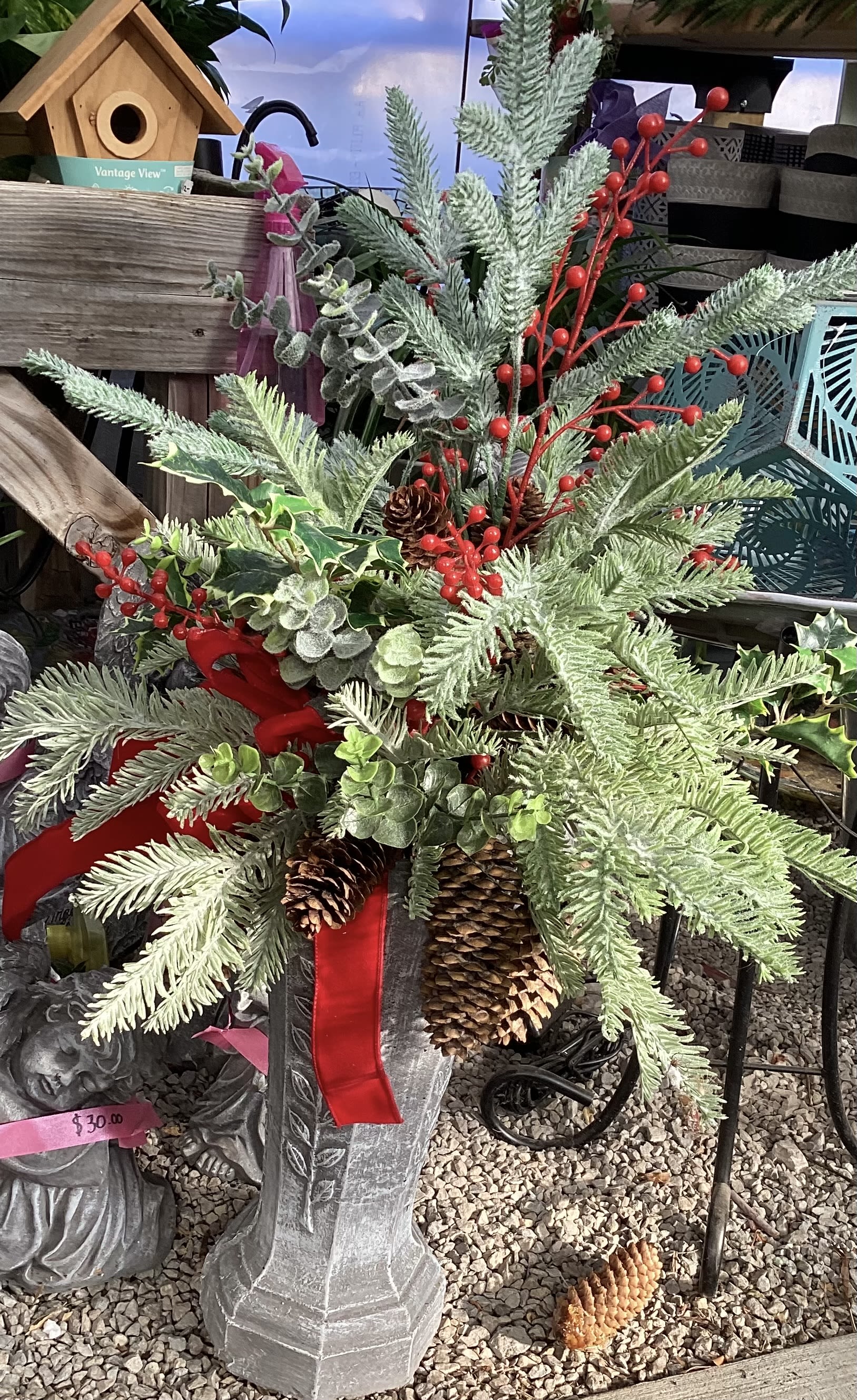 Festive standing arrangement - A bright festive arrangement featuring pine, pine cones, and pops of red on top of a beautiful stone stand.