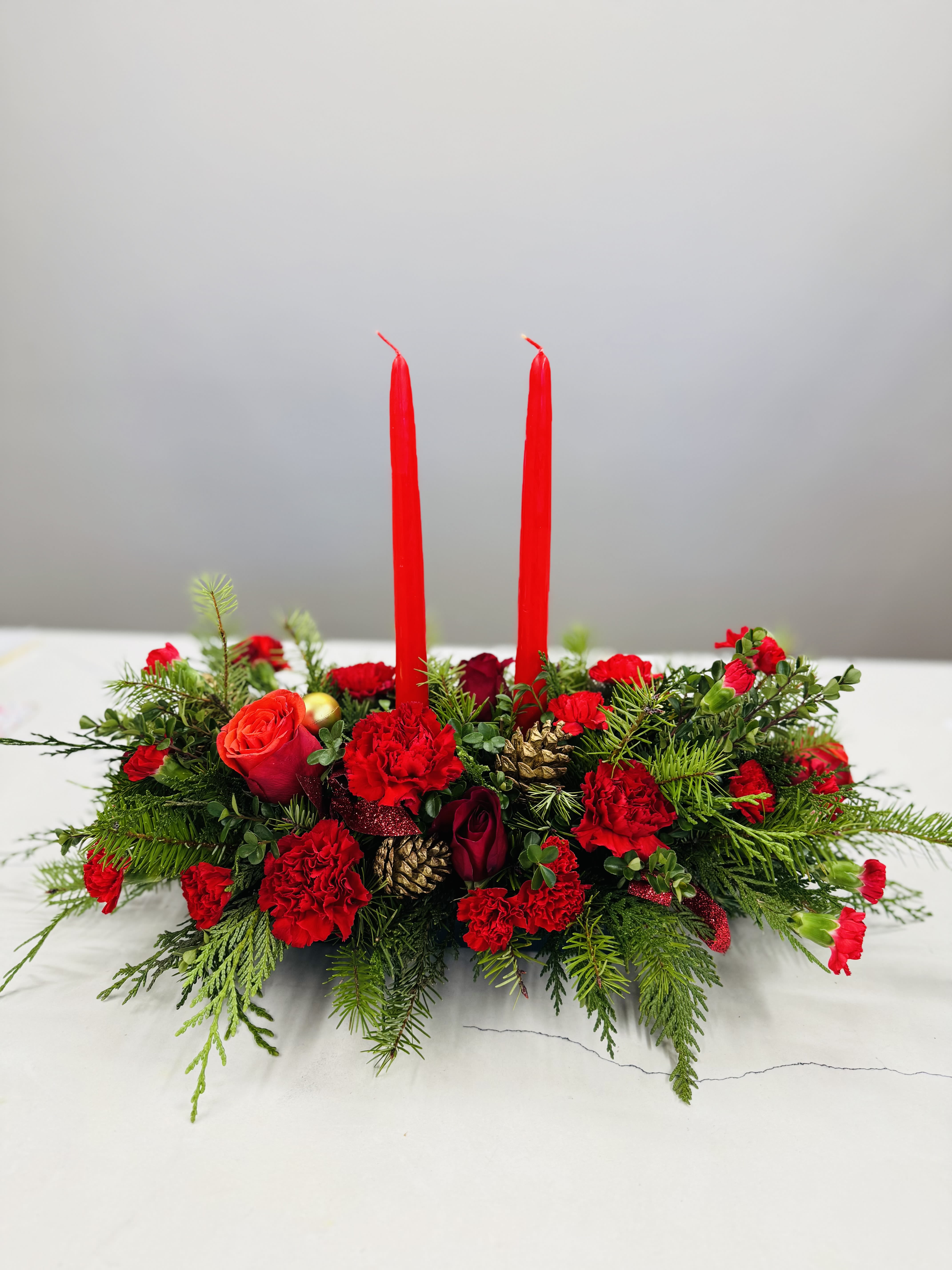 Winter wonderland glow - A festive Christmas centerpiece featuring lush evergreen foliage, vibrant red blooms, pinecone,and Twinkling candlelights- perfect for bringing warmth and holiday cheer to any table.