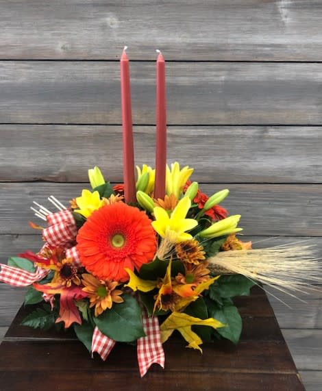 Picnic In Fall Centerpiece - Capture the warmth and charm of an autumn afternoon with our Picnic in Fall Centerpiece. This vibrant arrangement blends the bold elegance of lilies with the cheerful faces of gerbera and classic daisies. Richly colored fall leaves add seasonal texture, while lush greenery weaves everything together for a natural, freshly gathered look.  Perfect for dining tables, holiday gatherings, or adding a festive touch to any space, this centerpiece brings the cozy beauty of a fall picnic indoors—warm, welcoming, and wonderfully seasonal.  Flowers and colors may be substituted depending on availability and season.