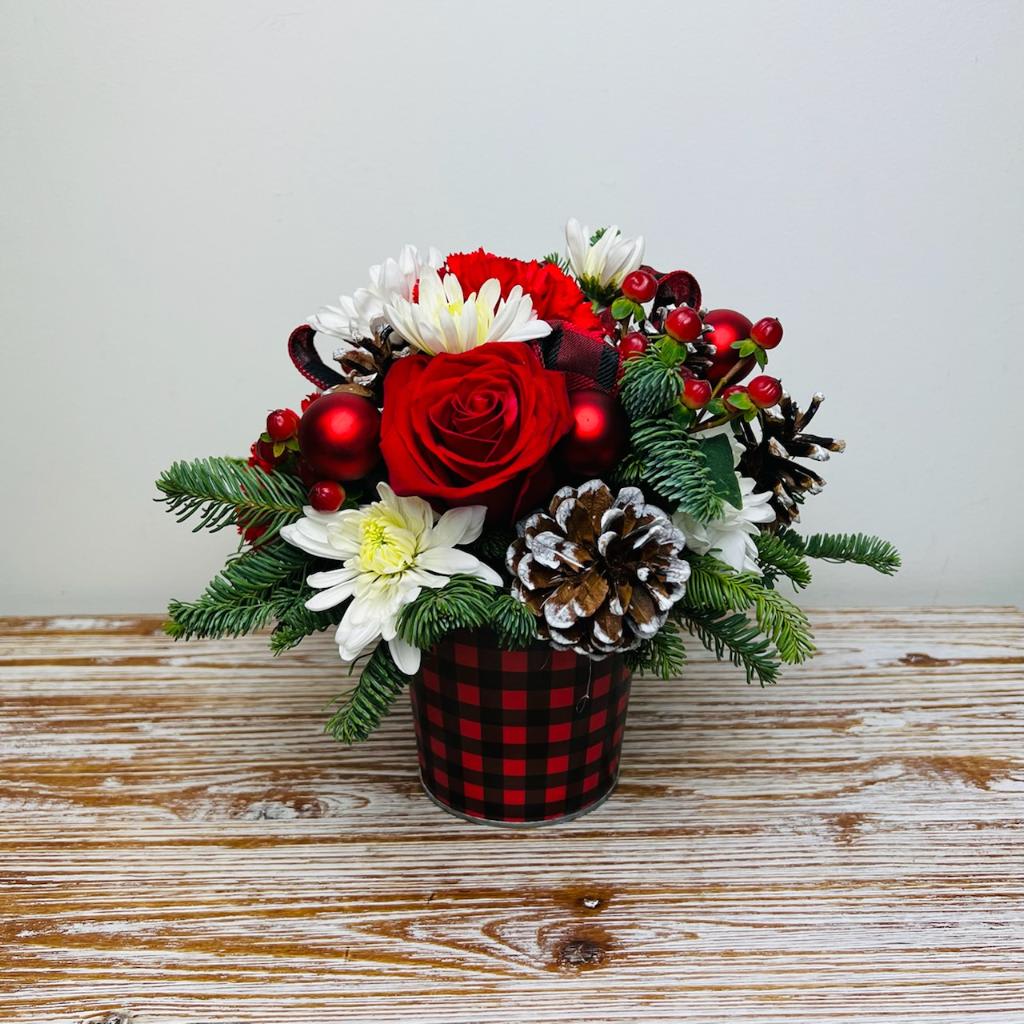 Country Holidays - With merry blooms and winter greens, our Country Holidays arrangement is accented with buffalo plaid ribbon, pinecones, and berries in a buffalo plaid tin container.  Approximately 10” Tall