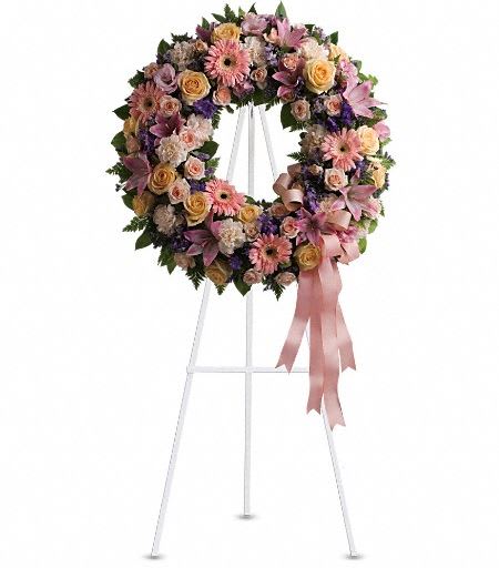 T239-1A Graceful Wreath - Family and friends will recollect how special their loved one was with this gentle and timeless circle of fragrant blooms to celebrate sweet memories. A mix of flowers such as peach roses, gerberas and carnations, pink asiatic lilies and lisianthus, purple limonium and lavender larkspur nest in greens on an easel-mounted wreath. Approximately 22 1/2&quot; W x 22 1/2&quot; H 