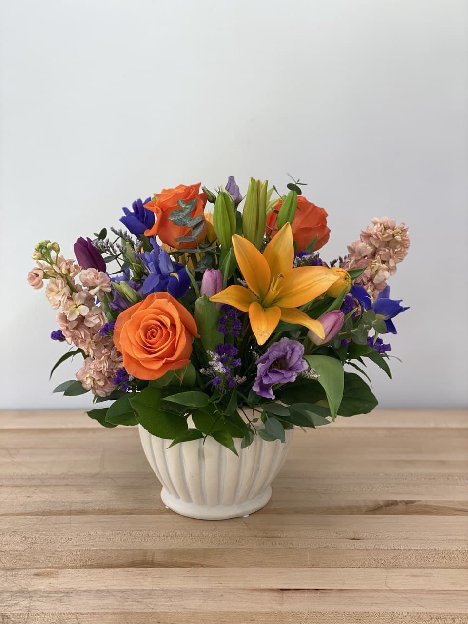 Orange Crush - An extraordinary combination of complementary purple and orange, including lilies, iris, lisianthus, roses, tulips, and stock in a gray washed ceramic container.