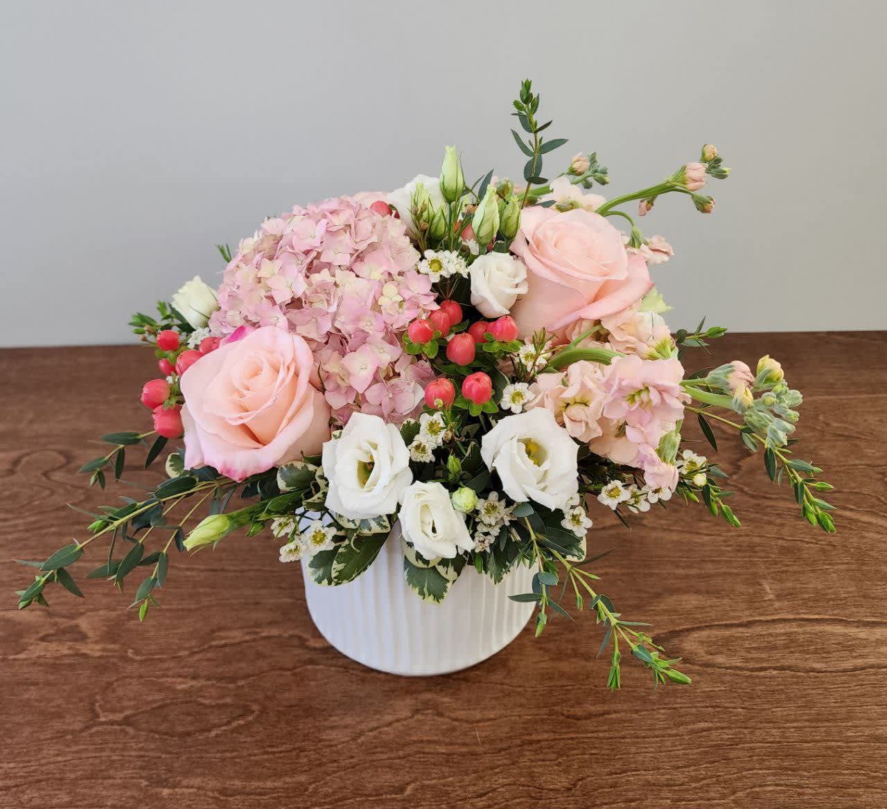 Spring Garden - Bring the softness and beauty of spring indoors with the Spring Garden! This luxurious combination of pink hydrangea, roses, lisianthus, stock, hypericum berries, and eucalyptus comes in a 5&quot; white textured cylinder vase.