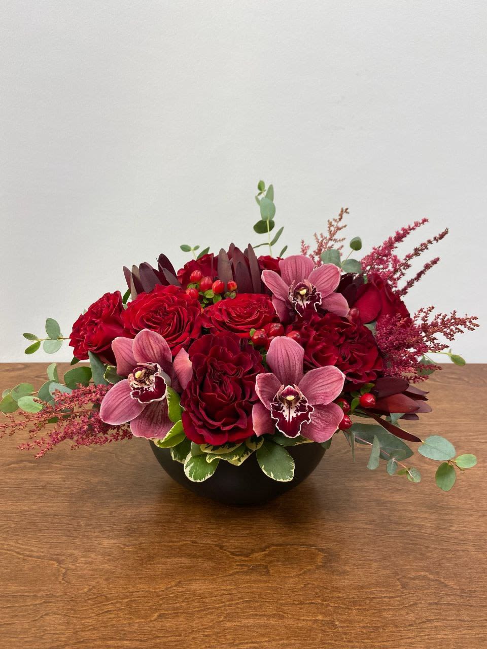 Velveteen - A sensuous, texturally indulgent arrangement of heart roses, pink cymbidium orchid, hypericum berry, astilbe, and safari in a black ceramic bowl. 