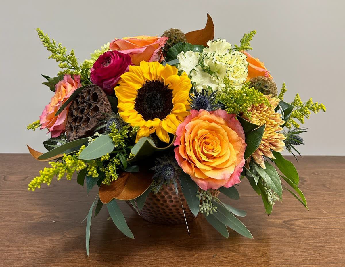 Gathered Centerpiece - This vibrant centerpiece will bring the beauty of fall to any gathering! Inspire your family and guests with this stunning combination of sunflowers, free spirit roses, kale, magnolia, and more. Comes in a round hammered copper vessel.