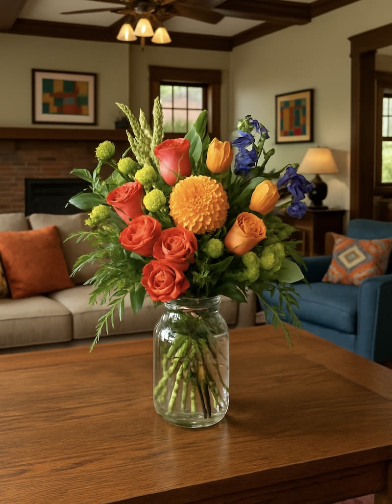 Auburn - NEW - Introducing the Auburn Arrangement – a vibrant autumn bouquet designed to bring warmth and elegance to any space. This stunning display features a premium orange dahlia, paired with lush roses, cheerful tulips, and seasonal greenery, all artfully arranged in a classic clear mason jar. Perfect for celebrations, anniversaries, or simply celebrating the beauty of fall, the Auburn arrangement captures the rich colors of the season in one unforgettable gift.