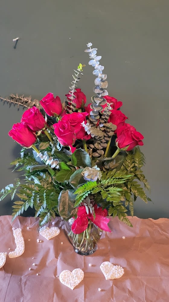 Romantic Harmony - This elegant floral arrangement showcases vibrant red roses beautifully complemented by lush greenery and delicate eucalyptus stems. Placed in a classic glass vase, it exudes natural charm and romance, making it a perfect centerpiece for any special occasion.        