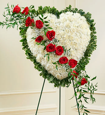 Always In My Heart - This beautiful floral tribute shows your undying love during this difficult time. This standing spray arrangement in the shape of a heart is created from fresh white carnations, red roses, Baby's Breath and more. Traditionally sent directly to the funeral home by family members or friends and displayed on a stand. Our florists use only the freshest flowers available so varieties and colors may vary. (Picture shown Premium)