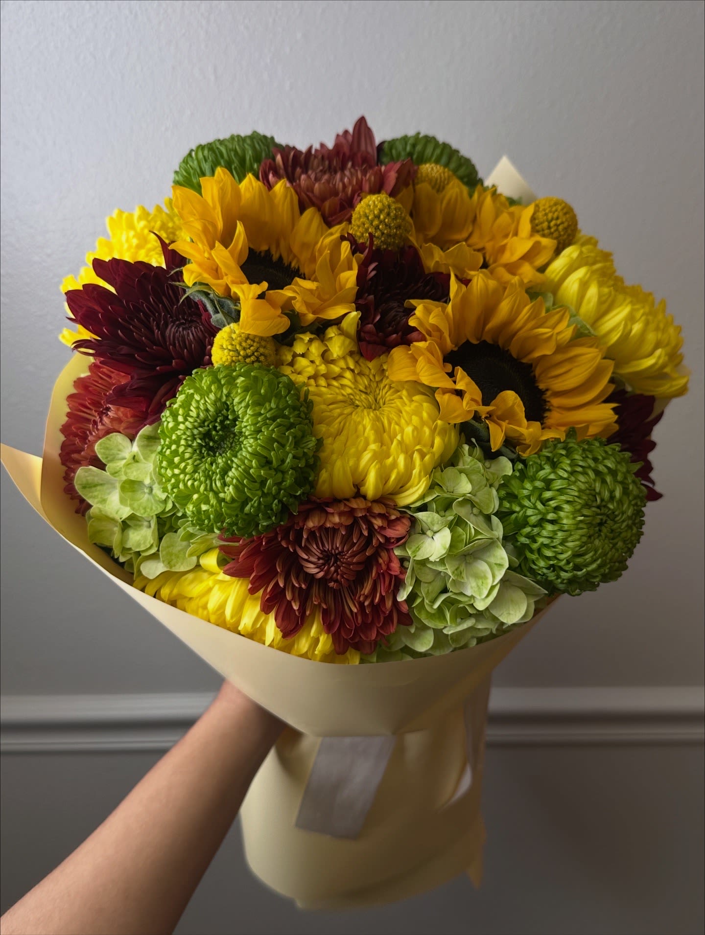 Vibrant Cheer - A vibrant, energetic bouquet featuring sunflowers, green and burgundy chrysanthemums, soft-toned hydrangeas, and golden billy balls that add texture and movement. The combination of bright yellows, fresh greens, and deep accents creates a warm, harmonious design—perfect for brightening any day and conveying joy, affection, and vitality. It's the perfect bouquet to bring joy to someone special in our lives. It also serves to show gratitude and appreciation.