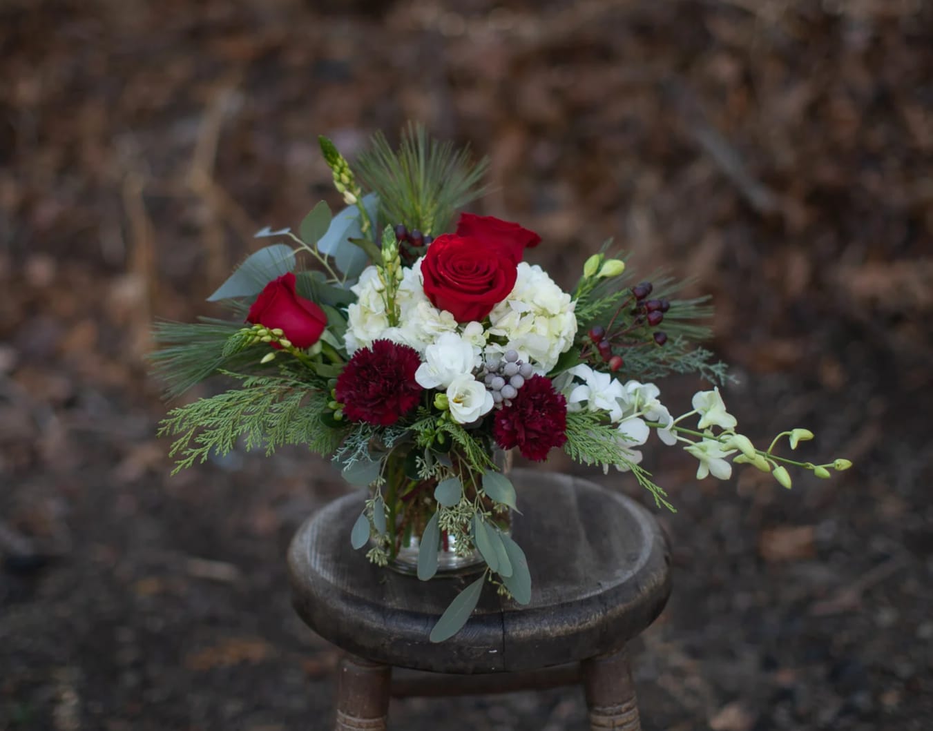 Cinnamon Cylinder - Burgundy tones add a cinnamon spice to traditional winter reds and white. A beautiful assortment of winter foliage with beautiful floral  varieties including hydrangea, roses, carnations and orchids. 