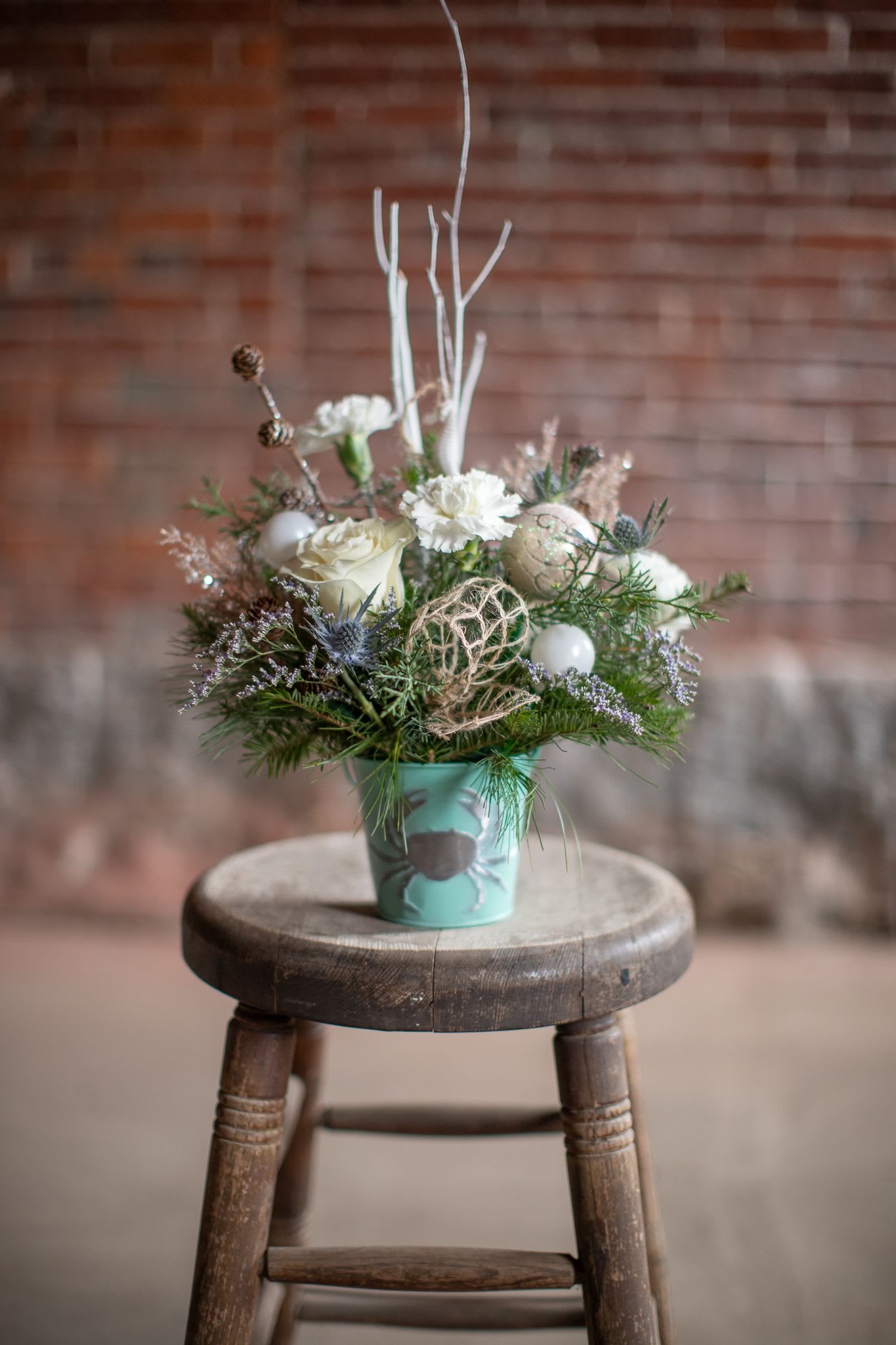 Coastal Christmas - Winter foliage is artfully arranged in a coastal inspired tin container. This arrangement comes with assorted ornaments either in the shape of sea horses or starfish hanging from winter birch branches. Adorned with glittering pinecones and artificial champagne cedar this design is sure to sing to the beach lovers heart. Created by Katie  