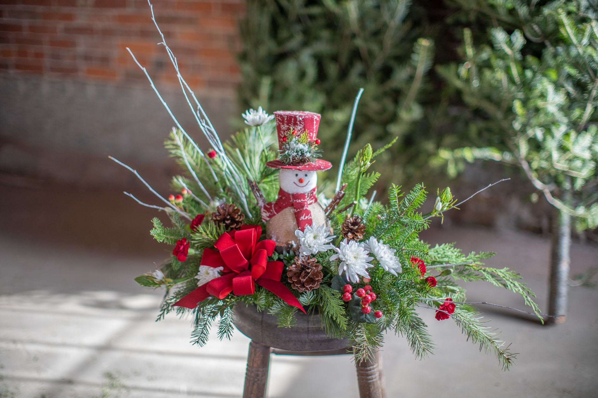 Magic in his hat - Remember how Frosty came to life when they placed the magic hat on his head. Just like the song goes this snowman is magic, well at least his hat is. Created in a design tray with fresh winter foliage, pine cones, and fresh flowers. The focal point being a keepsake snowman they can reuse every winter season. It's truly magical. 