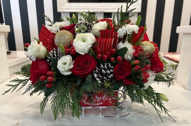 Santa's Sleigh Ride - This festive holiday arrangement is in a &quot;sleigh&quot; vessel filled with  and assortment of red and white premium flowers and a variety of elements such as, ornaments, pine cones and holiday ribbon. 