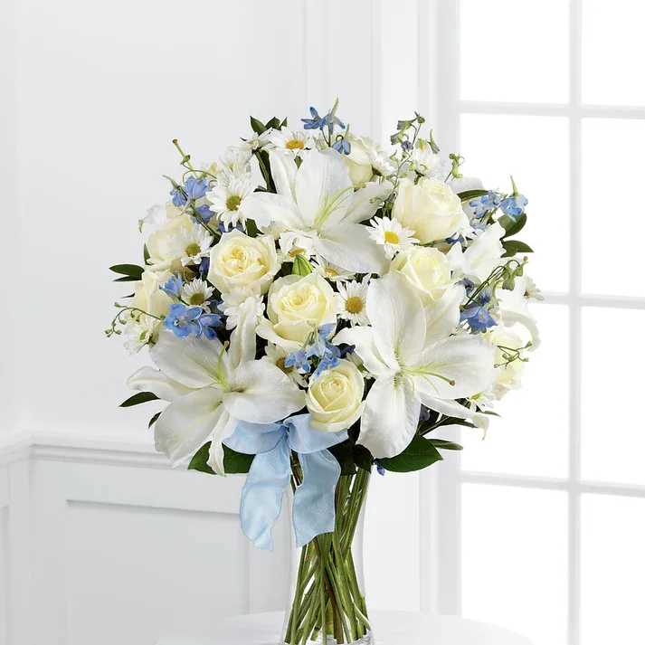 Sweet Peace Bouquet - Our Sweet Peace Bouquet is an elegant way to convey your deepest sympathies for the loss of a child. White roses, daisies, and Oriental lilies are sweetly accented with light blue delphinium, lush greens and a light blue organza ribbon, arranged to perfection in a clear glass vase, to create an exquisite way to offer comfort during this time of grief and sadness.   Details Premium arrangement is approximately 23" H x 18" W