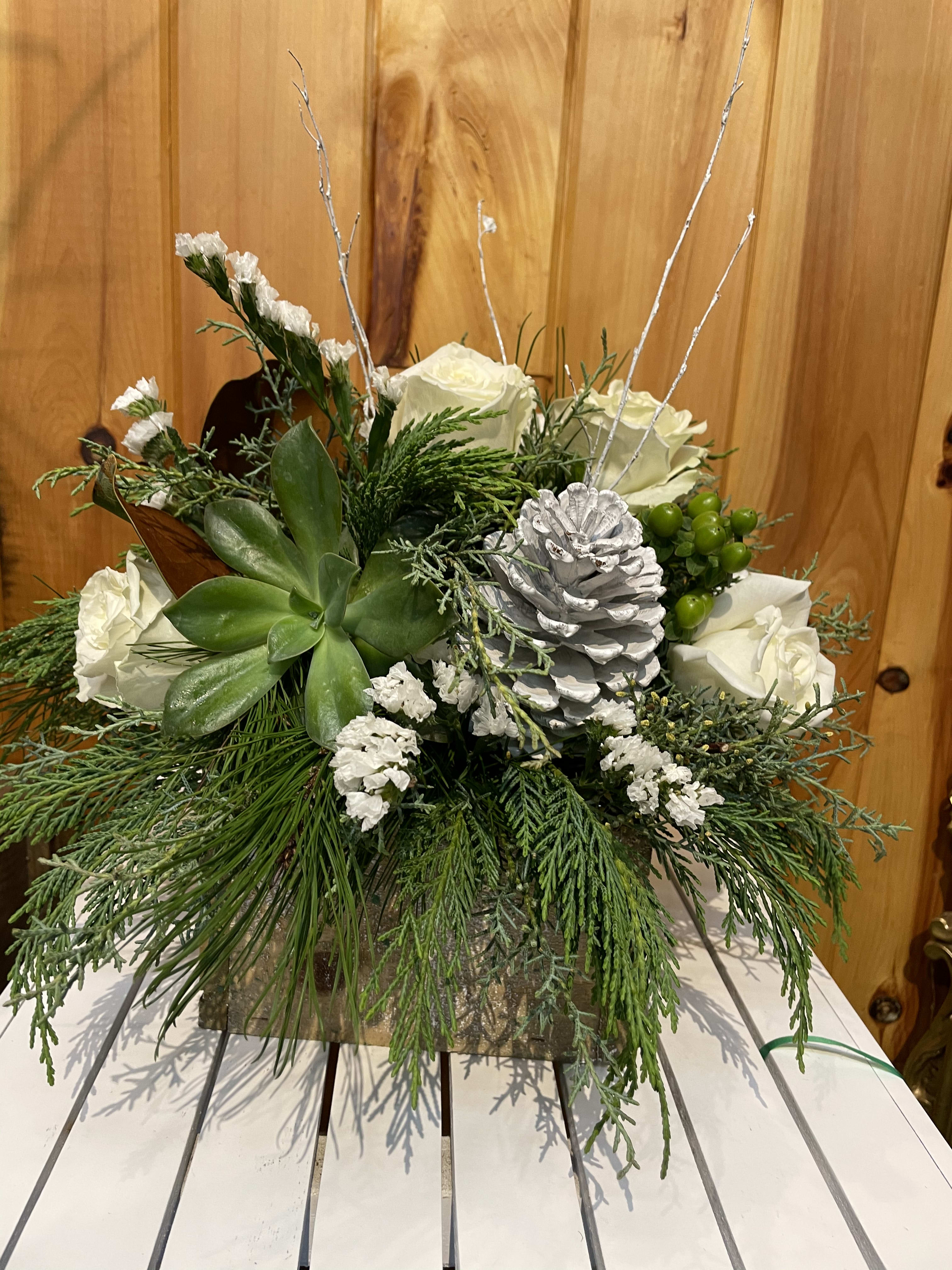 Winter White - A holiday arrangement in a natural container, with pine cones, roses and a variety of winter greens.