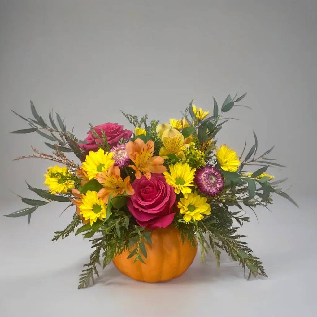 Autumn Radiance Pumpkin - Celebrate fall with a burst of color in our Autumn Radiance Pumpkin floral arrangement. This eye-catching centerpiece features a bright orange ceramic pumpkin overflowing with a unique and lively mix of hot pink roses, alstroemeria, yellow daisies, delicate dried flowers in shades of cranberry, lush evergreens, and fresh eucalyptus.  Handcrafted to bring a modern twist to traditional fall décor, this arrangement blends warm autumn tones with unexpected pops of vibrant color, making it perfect for Thanksgiving tables, seasonal home accents, or as a memorable fall gift.  Each bouquet is carefully designed with premium fresh and dried flowers, delivered with care throughout East Moline and surrounding areas. Add a bold splash of festive cheer to your autumn celebrations with this stunning pumpkin centerpiece.  Order your Autumn Radiance Pumpkin today and brighten your home with the perfect mix of classic fall warmth and lively color.  Appropriately 10”x10”