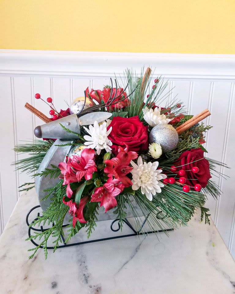 Sleigh Ride Splendor - This festive floral arrangement, featuring red and white blooms, is beautifully arranged in a charming sleigh-shaped container. With decorative touches like cinnamon sticks, red berries, and  glittery ornament, it captures the essence of holiday cheer and elegance. approx 13 X 12